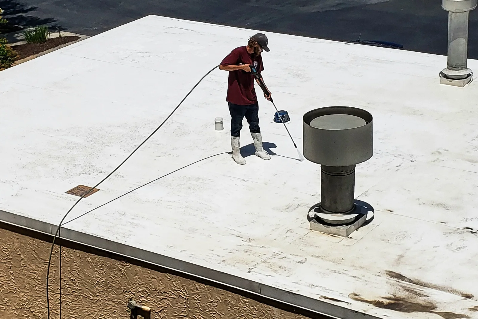 flat-roof-replacement-phoenix-worn-roof-coating A worker recoating a sun-worn white flat roof against a stucco parapet wall in Phoenix, the kind of surface staining and wear that signals it may be time for full flat roof replacement.