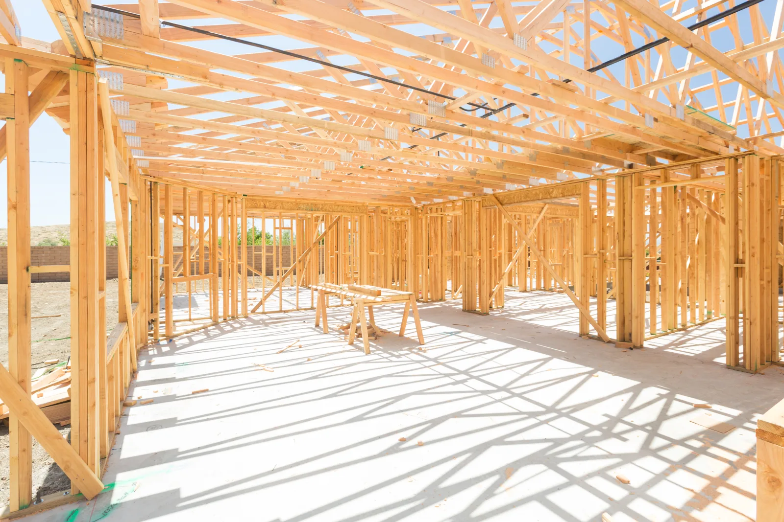 framing-contractors-phoenix-az-roof-truss-installation A Phoenix framing crew installing roof trusses over new wall framing on a home addition under a clear desert sky.