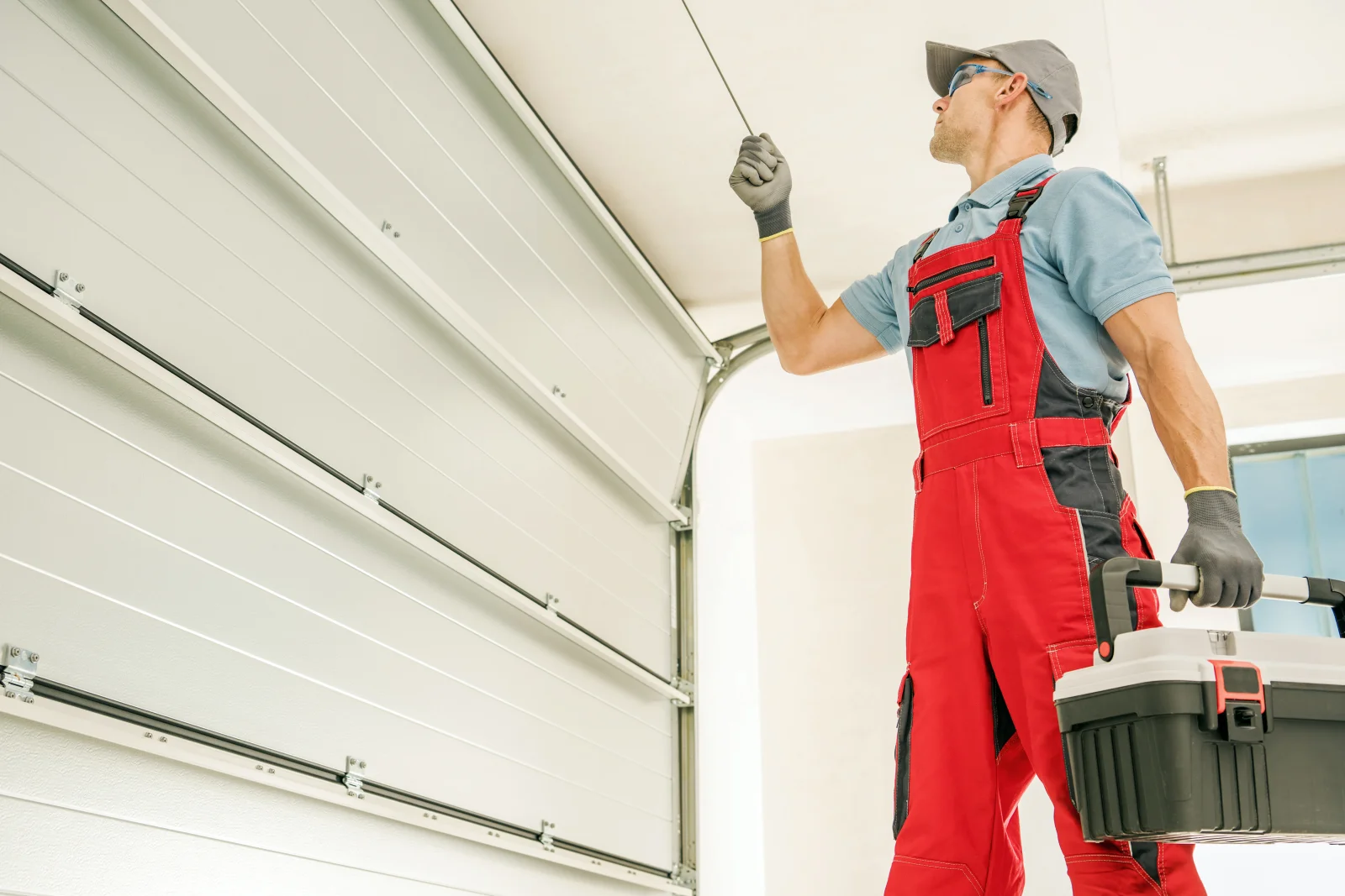 A technician in work overalls inspecting a garage door cable and roller assembly during a Phoenix tune-up visit.