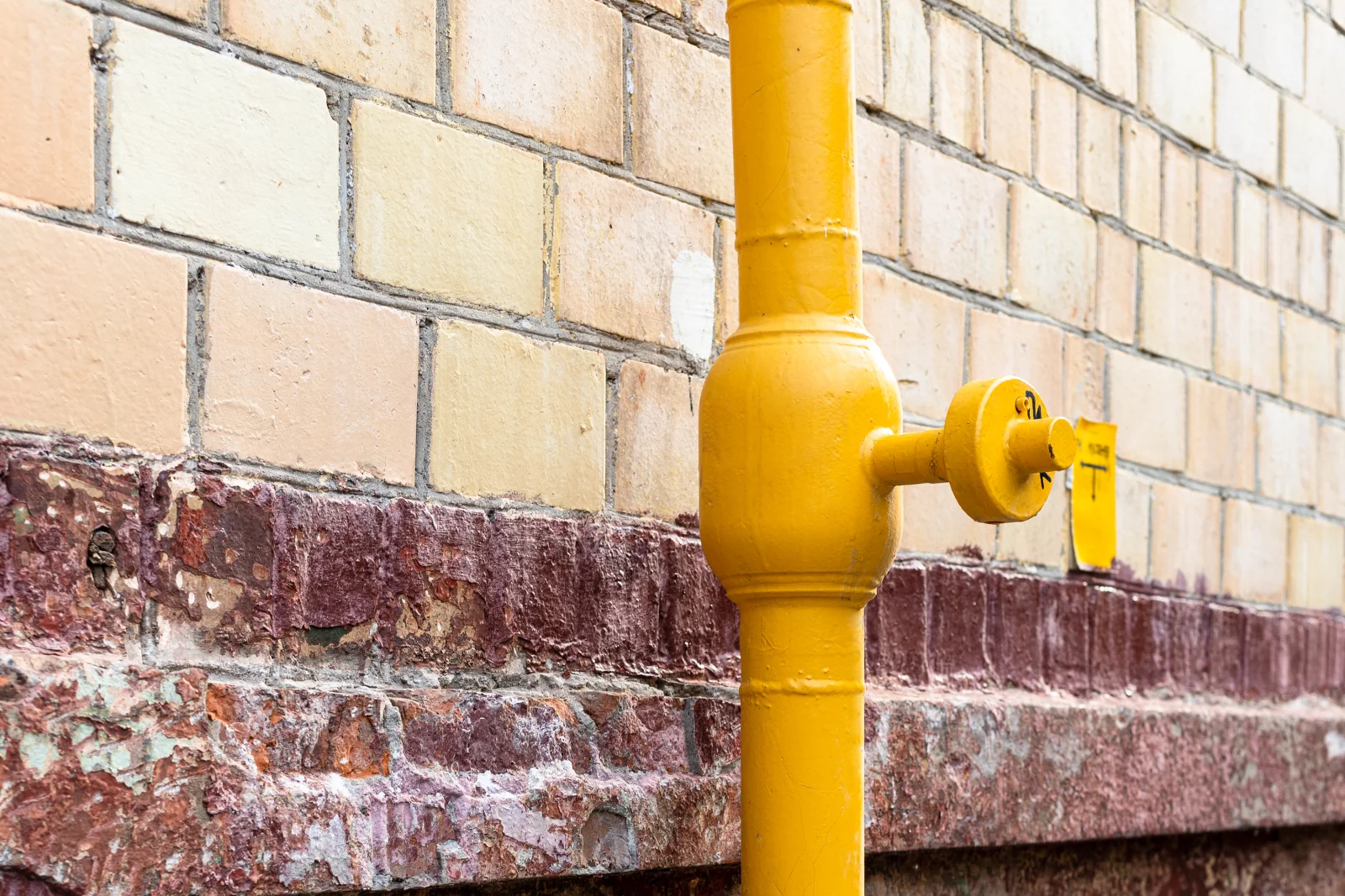 Gas line repair in Phoenix, Arizona — a yellow gas line and valve fitting running along the exterior brick wall of a home.