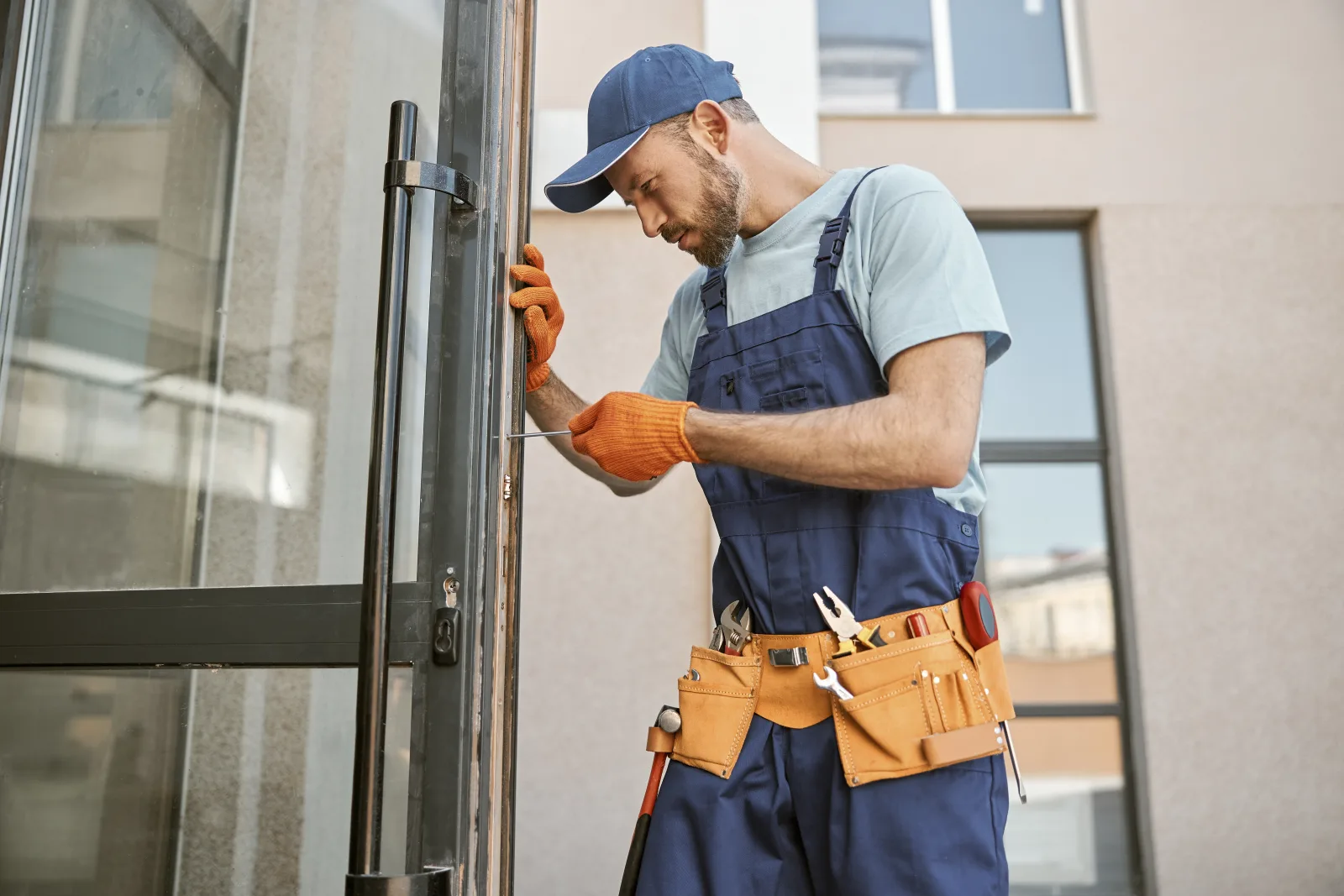 glass-door-repair-phoenix-technician-fixing-sliding-door Glass door repair in Phoenix, Arizona — a technician in a tool belt repairing the hardware on a sliding glass patio door at a home's exterior.