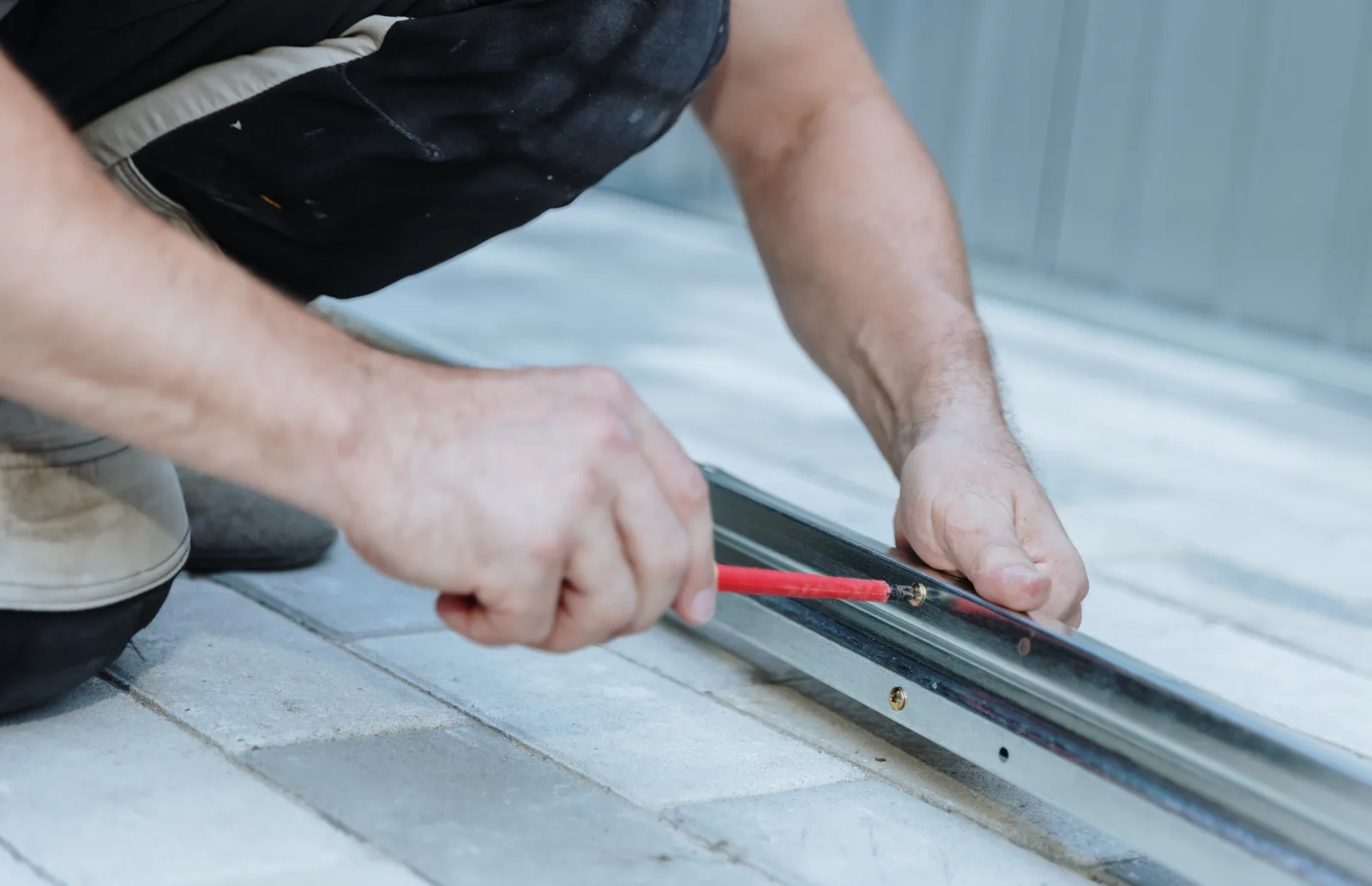 glass-door-repair-phoenix-roller-track-adjustment Glass door repair in Phoenix, Arizona — a technician kneeling to adjust a sliding glass door track and roller with a screwdriver.