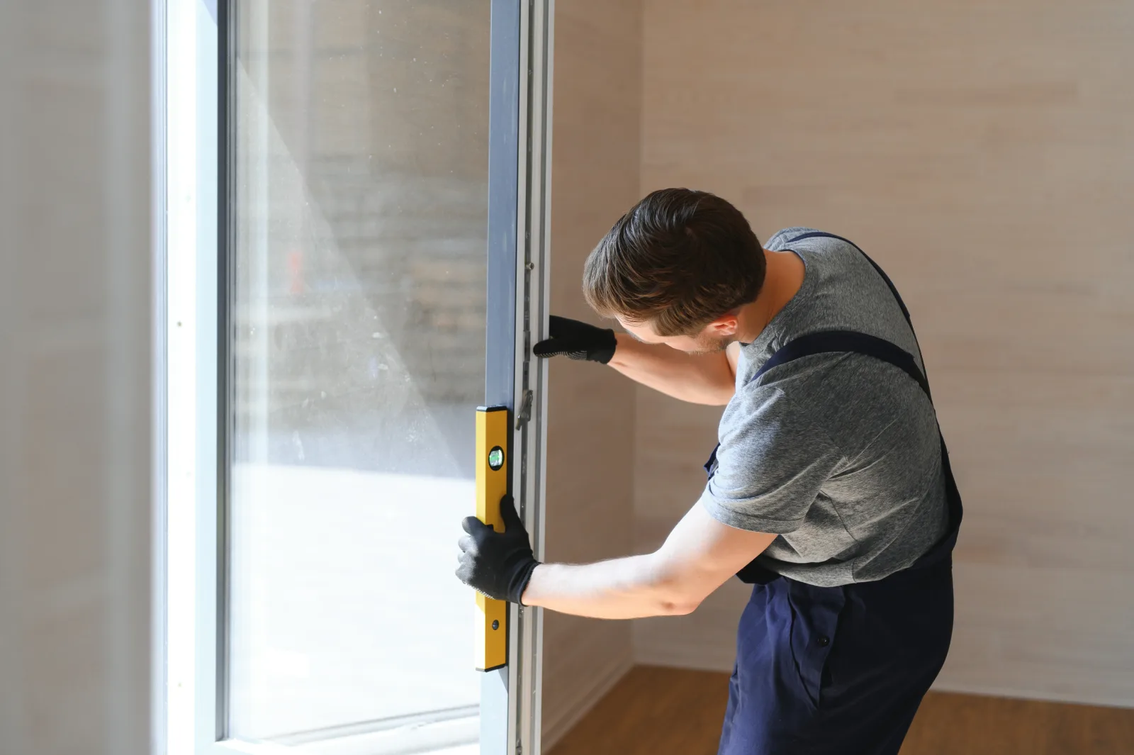glass-door-repair-phoenix-track-frame-alignment-check Glass door repair in Phoenix, Arizona — a technician using a level to check a sliding glass door frame for plumb before adjusting the track.