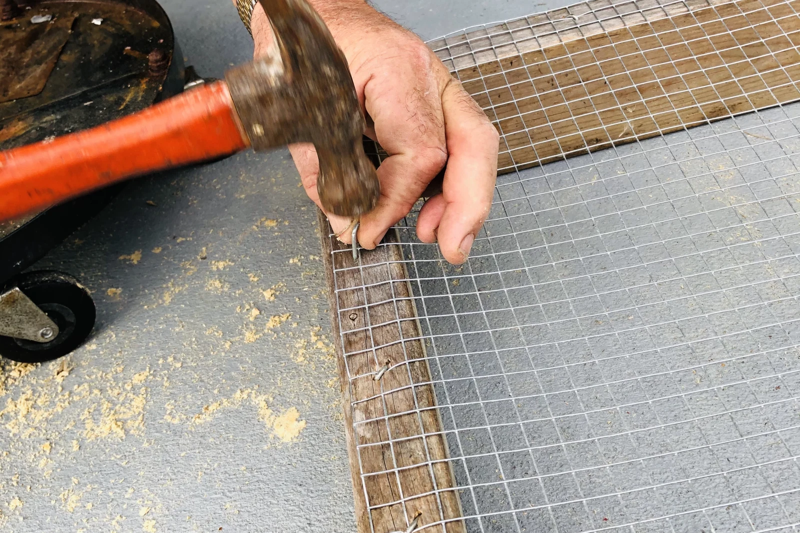 A pest-control technician nailing hardware-cloth exclusion wire to a raised bed frame, the kind of buried barrier a gopher control pro installs to protect Phoenix planting beds and irrigation lines.