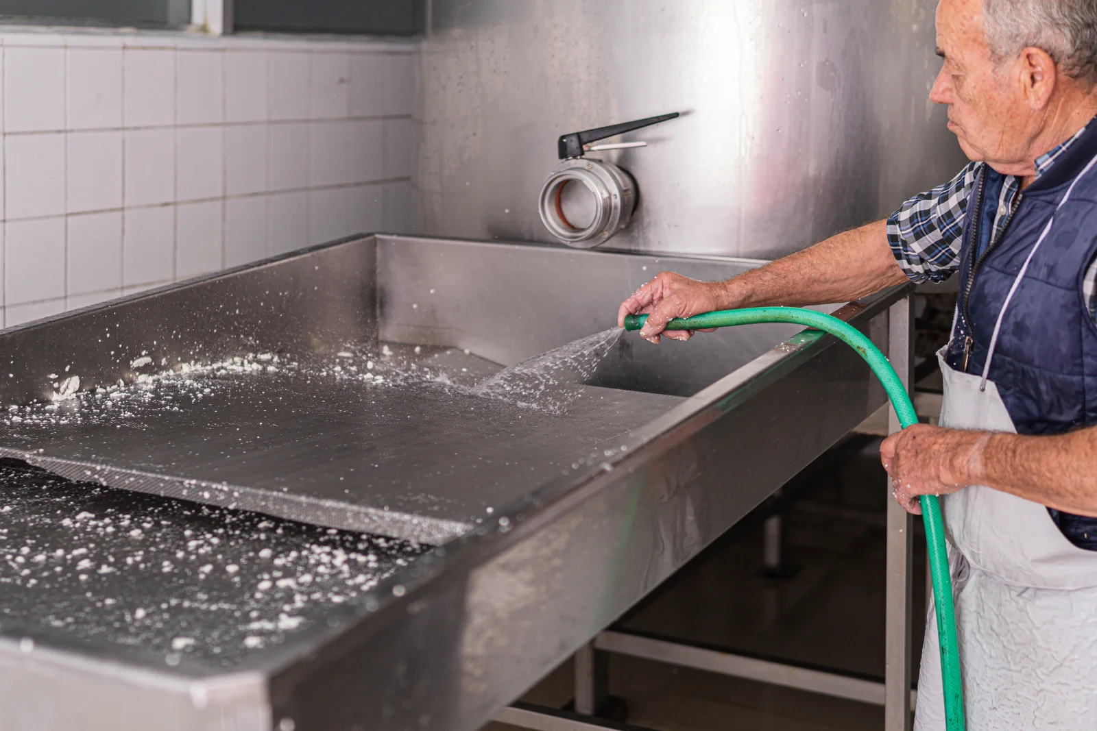 grease-trap-cleaning-phoenix-technician-hosing-down-commercial-kitchen-trap Grease trap cleaning in Phoenix, Arizona — a technician in a work apron hosing down a stainless steel grease trap basin in a commercial kitchen.