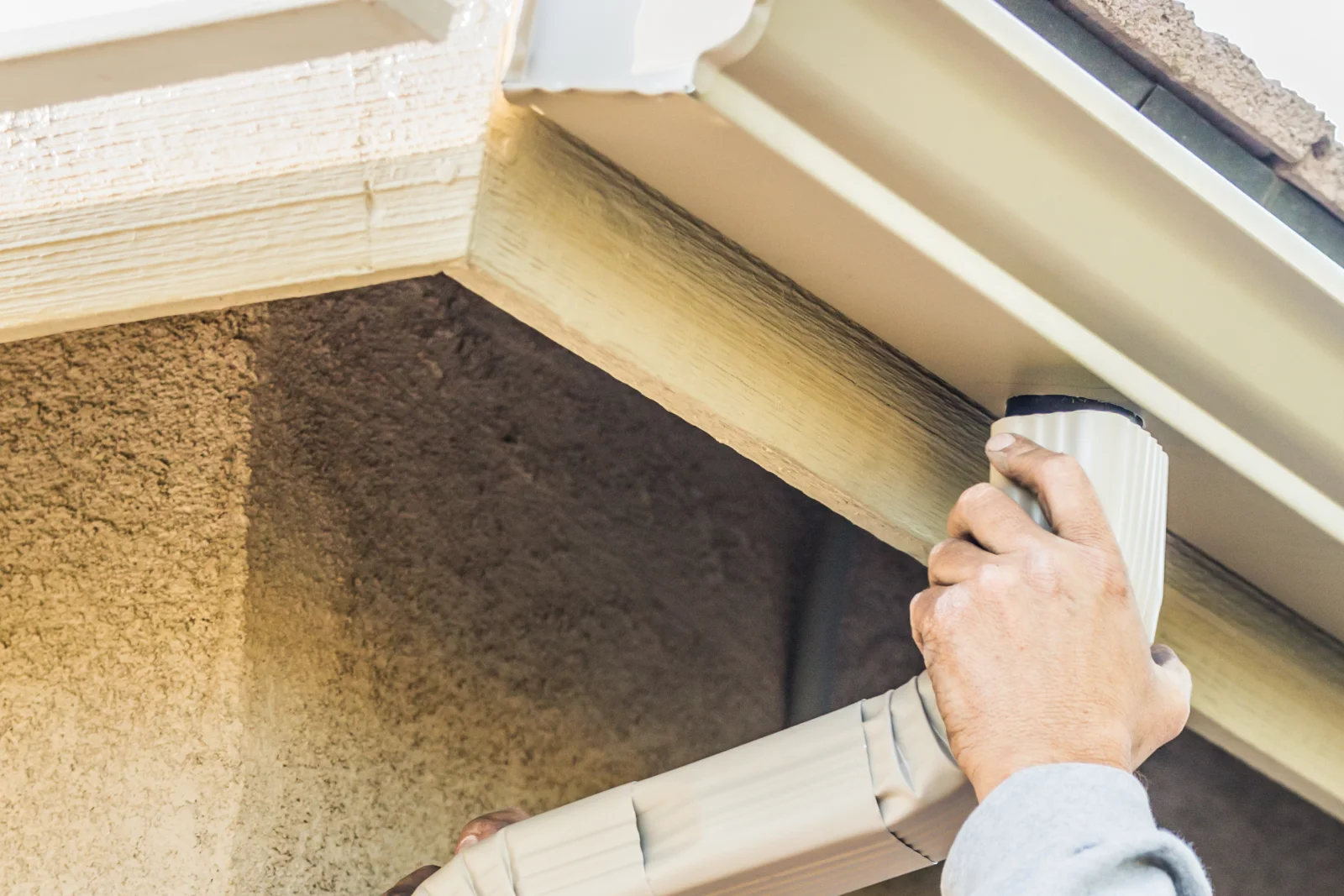 A technician attaching a downspout elbow to a stucco Phoenix home during a gutter installation.