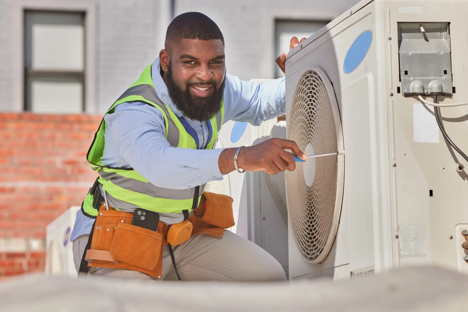 heat-pump-installation-phoenix-technician-outdoor-condenser Heat pump installation in Phoenix, Arizona — a smiling HVAC technician in a safety vest installing a new outdoor heat pump condenser.