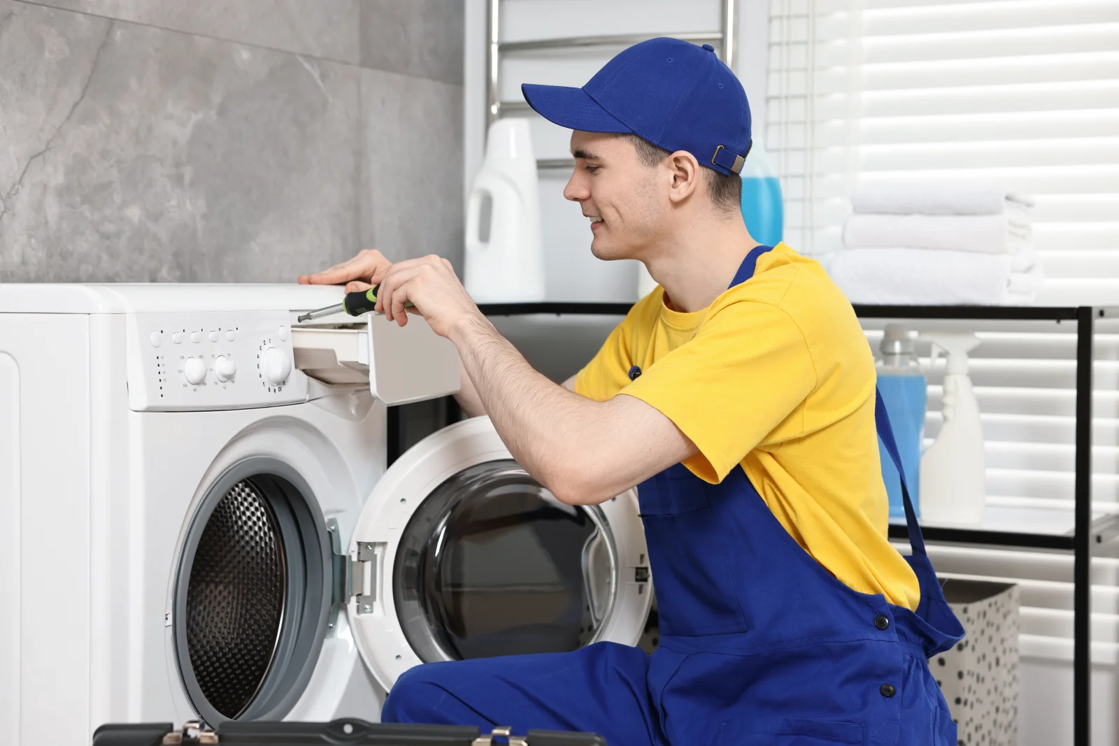 home-appliance-repair-phoenix-washer-dryer-repair A technician using a screwdriver to repair a front-load washing machine in a Phoenix, Arizona laundry room, the kind of repair-or-replace call a vetted Phoenix pro helps homeowners make.