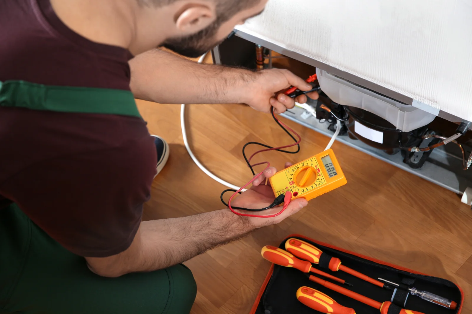 home-appliance-repair-phoenix-refrigerator-diagnosis A technician using a multimeter to diagnose a refrigerator in a Phoenix, Arizona kitchen, the kind of same-day appliance diagnosis a vetted Phoenix pro provides.
