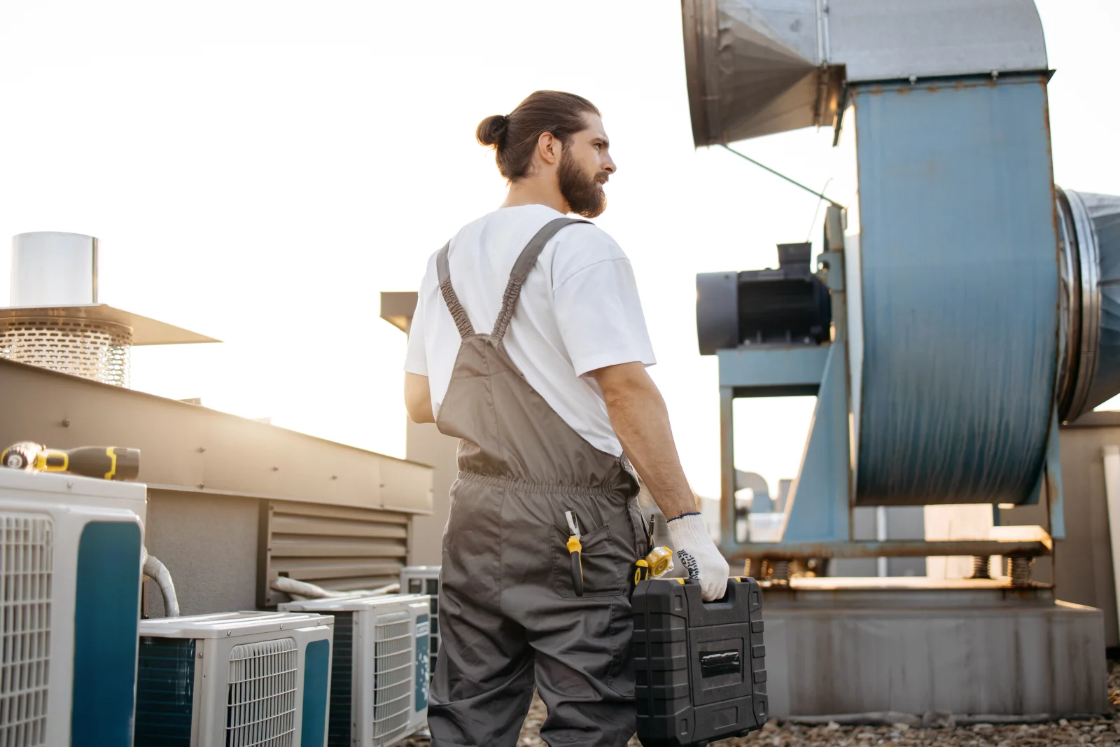 A technician arriving at a rooftop exhaust fan with his tool case during a Phoenix commercial hood cleaning service call, the duct-to-fan work a surface-only wipe-down skips.