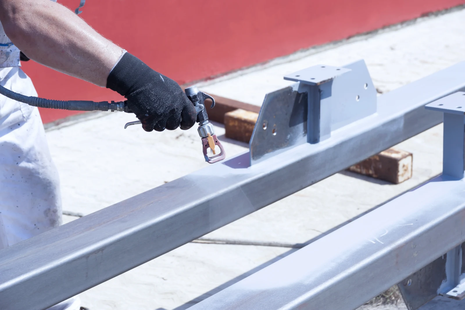 industrial-paint-contractors-phoenix-corrosion-coating A contractor in coveralls spray-applying corrosion-resistant coating to structural steel beams and brackets at a Phoenix, Arizona job site.