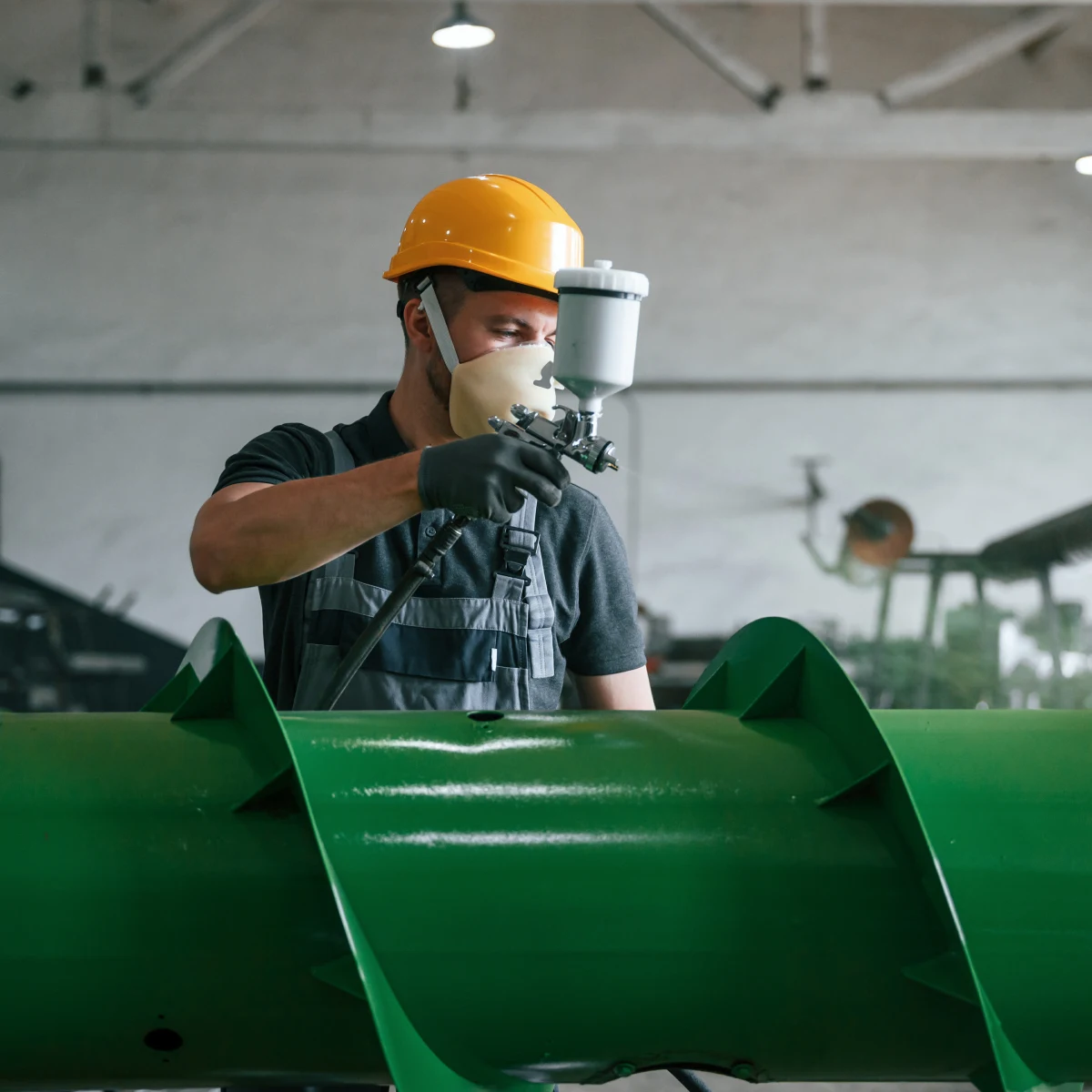 industrial-paint-contractors-phoenix-contractor Industrial paint contractors in Phoenix, Arizona — a coatings contractor in a respirator, safety glasses, and coveralls applying protective coating in an industrial facility.