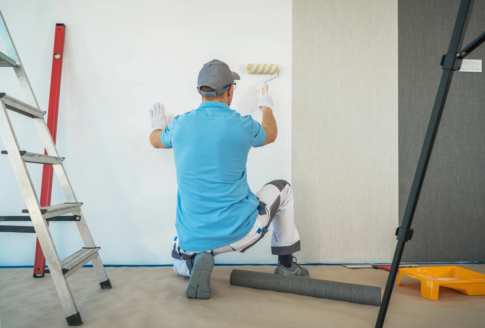 A Phoenix interior painter in gloves and knee protection carefully rolling paint along a wall edge.