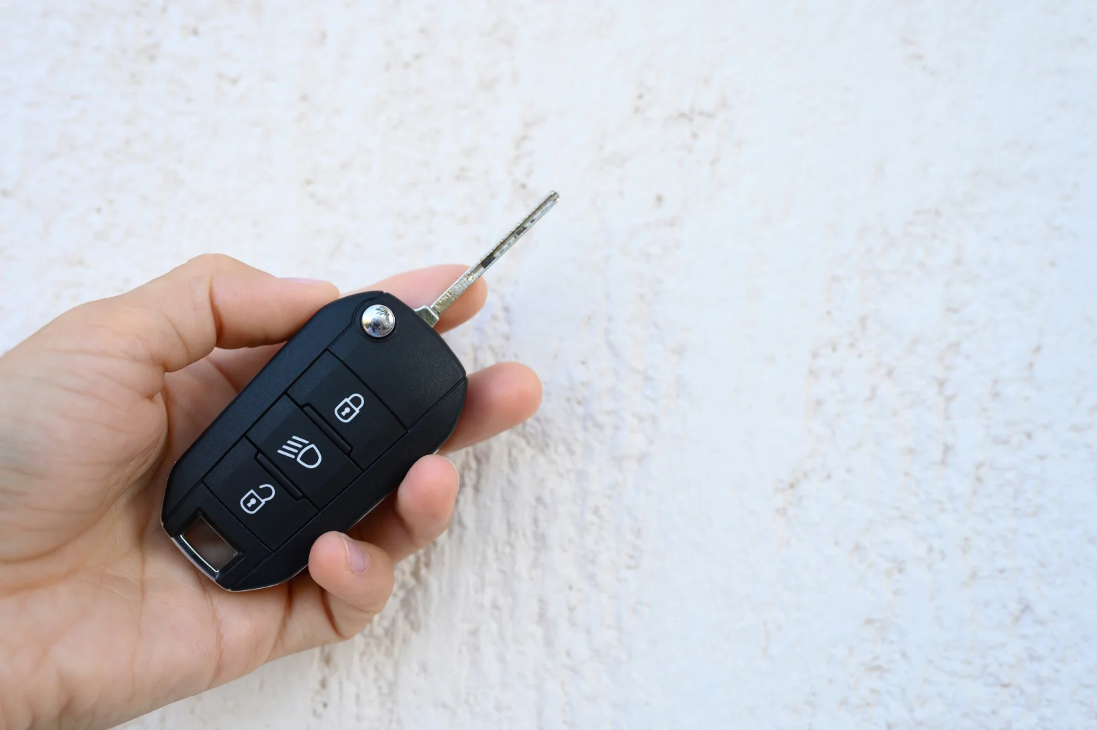 A hand holding a car key fob against a sunlit stucco wall in Phoenix, where extreme summer heat breaks down fob housings and electronics until they need replacing.