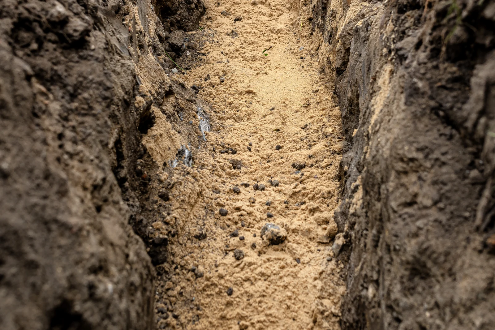 landscape-drainage-phoenix-desert-conditions A close-up view down a freshly dug drainage trench showing the hard, compacted layers of desert soil a Phoenix drainage pro has to cut through.