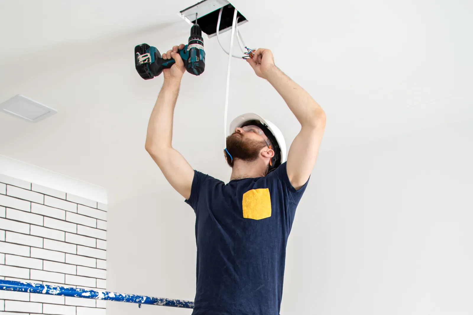 licensed-handyman-phoenix-ceiling-fan-install A handyman in a hard hat and work uniform installing a ceiling light fixture in a Phoenix home.