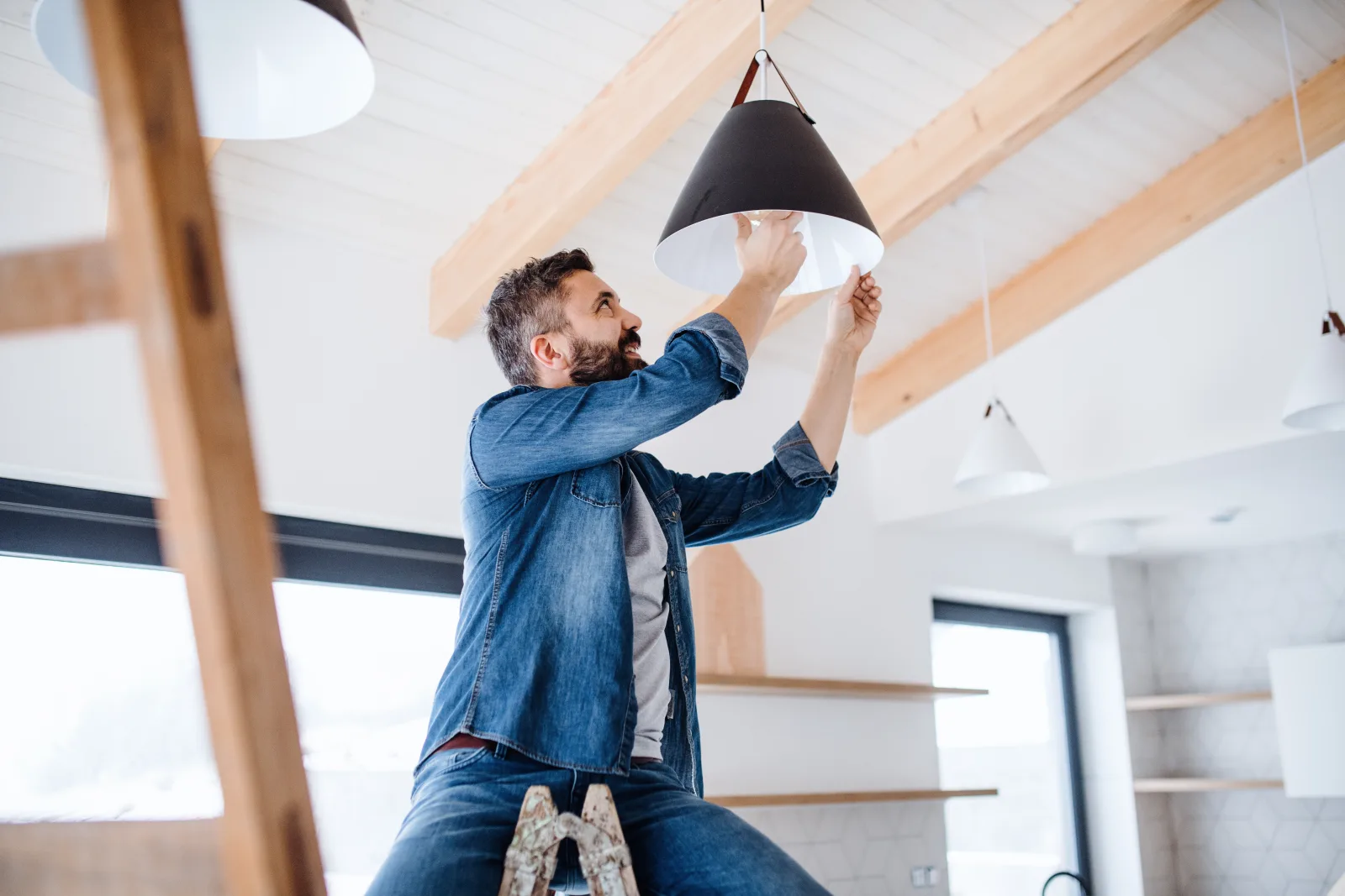 An electrician installing a new light fixture on the ceiling of a Phoenix home during a repair visit.