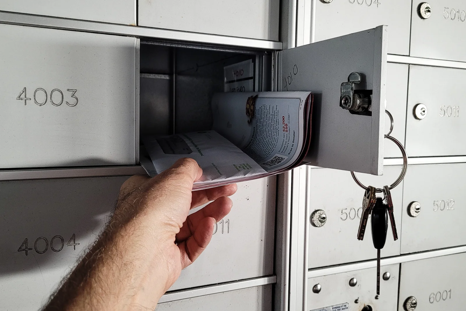 Mailbox locksmith in Phoenix, Arizona — a hand retrieving mail from an open cluster mailbox compartment with keys still in the lock.