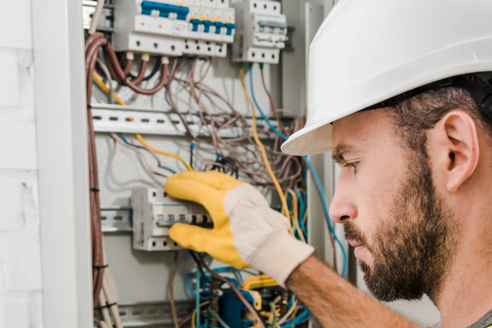 North Phoenix electrician — an electrician in a hard hat and glove inspecting wiring inside a breaker panel.