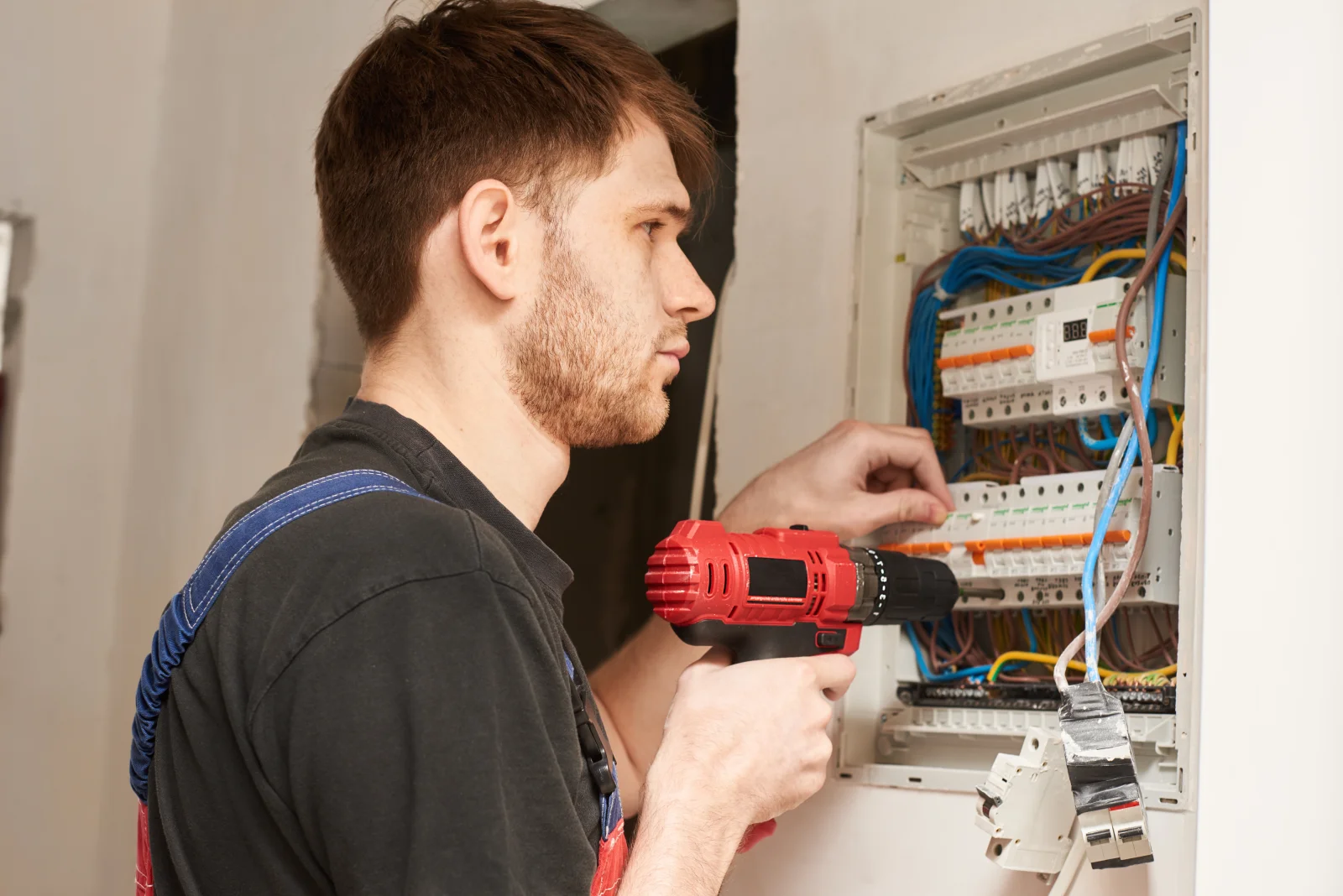 North Phoenix electrician — an electrician in work coveralls repairing a breaker panel with a drill.