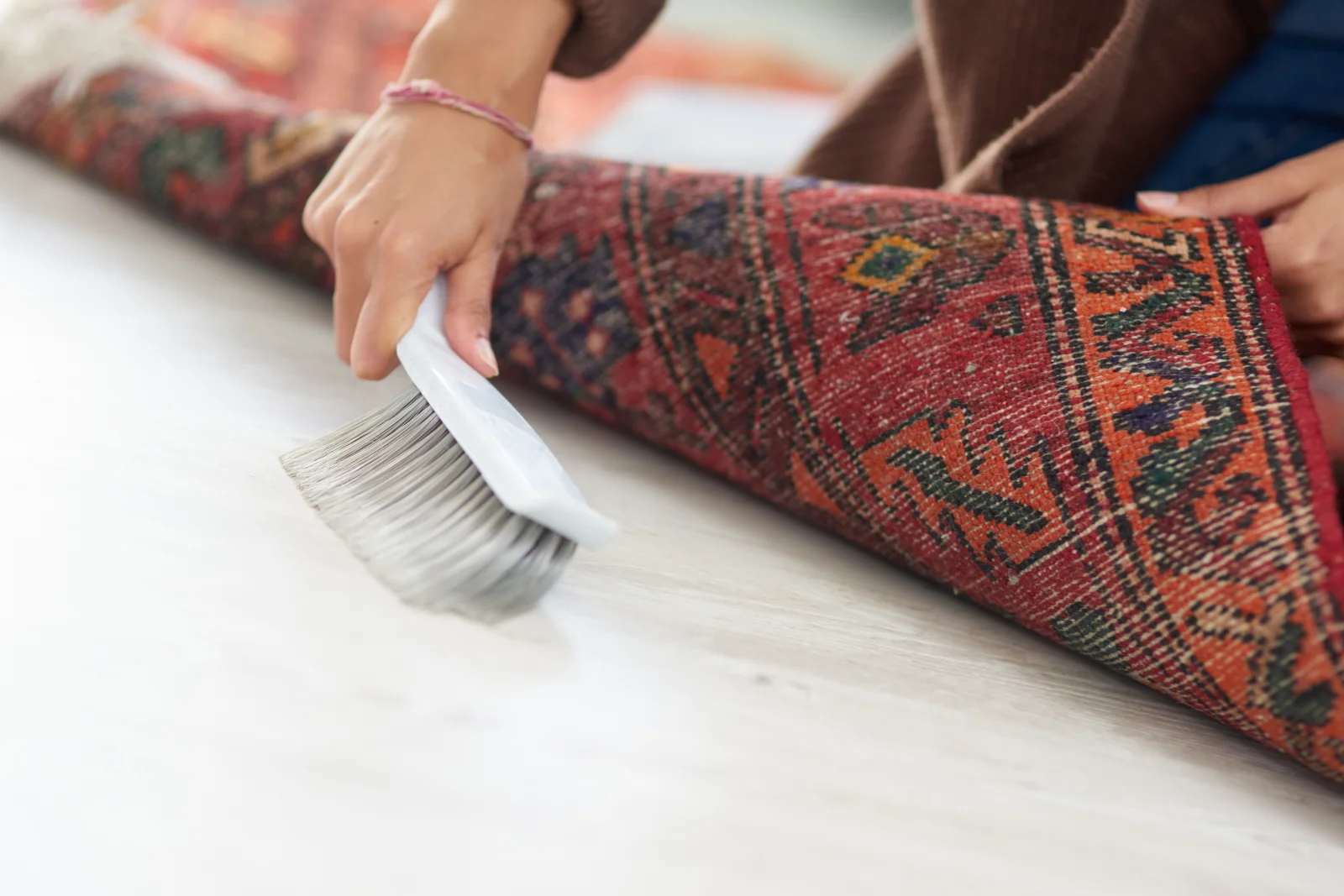 A hand hand-brushing the fringe of a rolled hand-knotted oriental rug during professional cleaning in Phoenix.