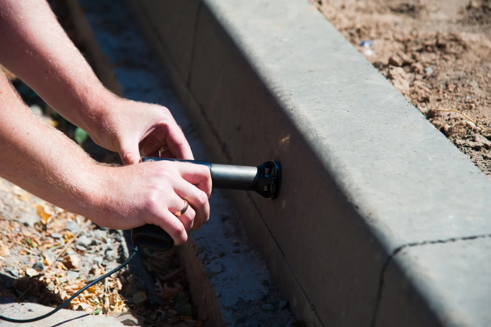 outdoor-lighting-installation-phoenix-low-voltage-wire-connection Outdoor lighting installation in Phoenix, Arizona, an electrician connecting a low-voltage landscape lighting wire splice along a paver edge.