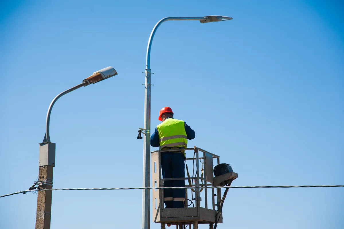 parking-lot-lighting-repair-phoenix-electrician-servicing-pole-light-from-lift Parking lot lighting repair in Phoenix, Arizona — an electrician in a hard hat and hi-vis vest servicing a parking lot light pole from an aerial lift.