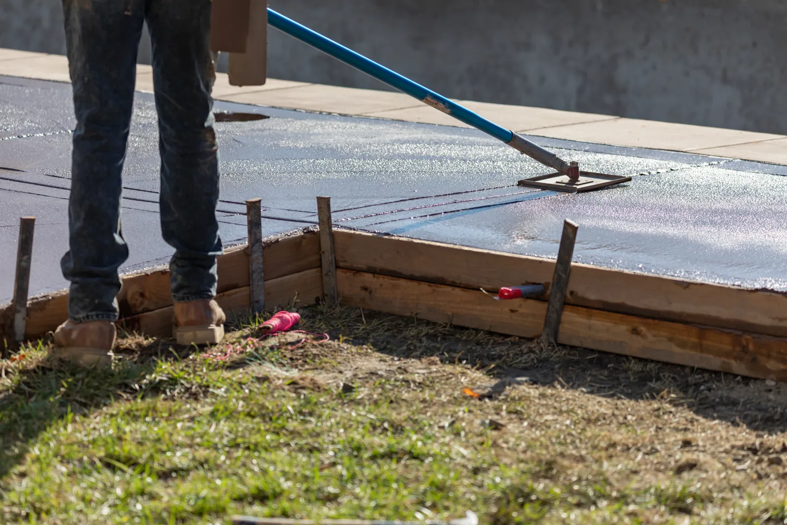 patio-builders-phoenix-az-concrete-slab-finishing A patio builder in Phoenix, Arizona bull-floating a freshly poured concrete patio slab inside staked wood forms before the surface finish is applied.