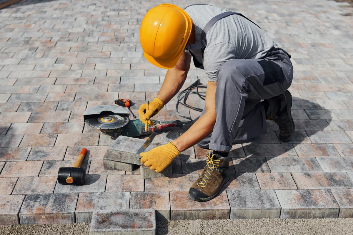patio-builders-phoenix-az-crew-cutting-pavers Patio builders in Phoenix, Arizona — a crew member in a hard hat and work gloves cutting and setting pavers for a new backyard patio.