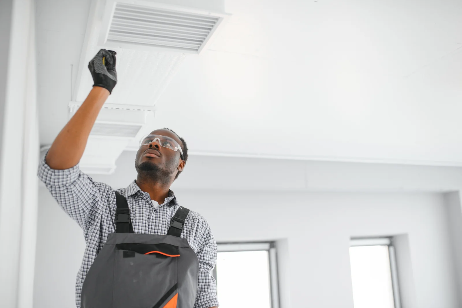 phoenix-duct-cleaning-vent-inspection An HVAC technician in safety glasses and gloves inspecting a ceiling supply vent in a Phoenix home before cleaning the ductwork behind it.
