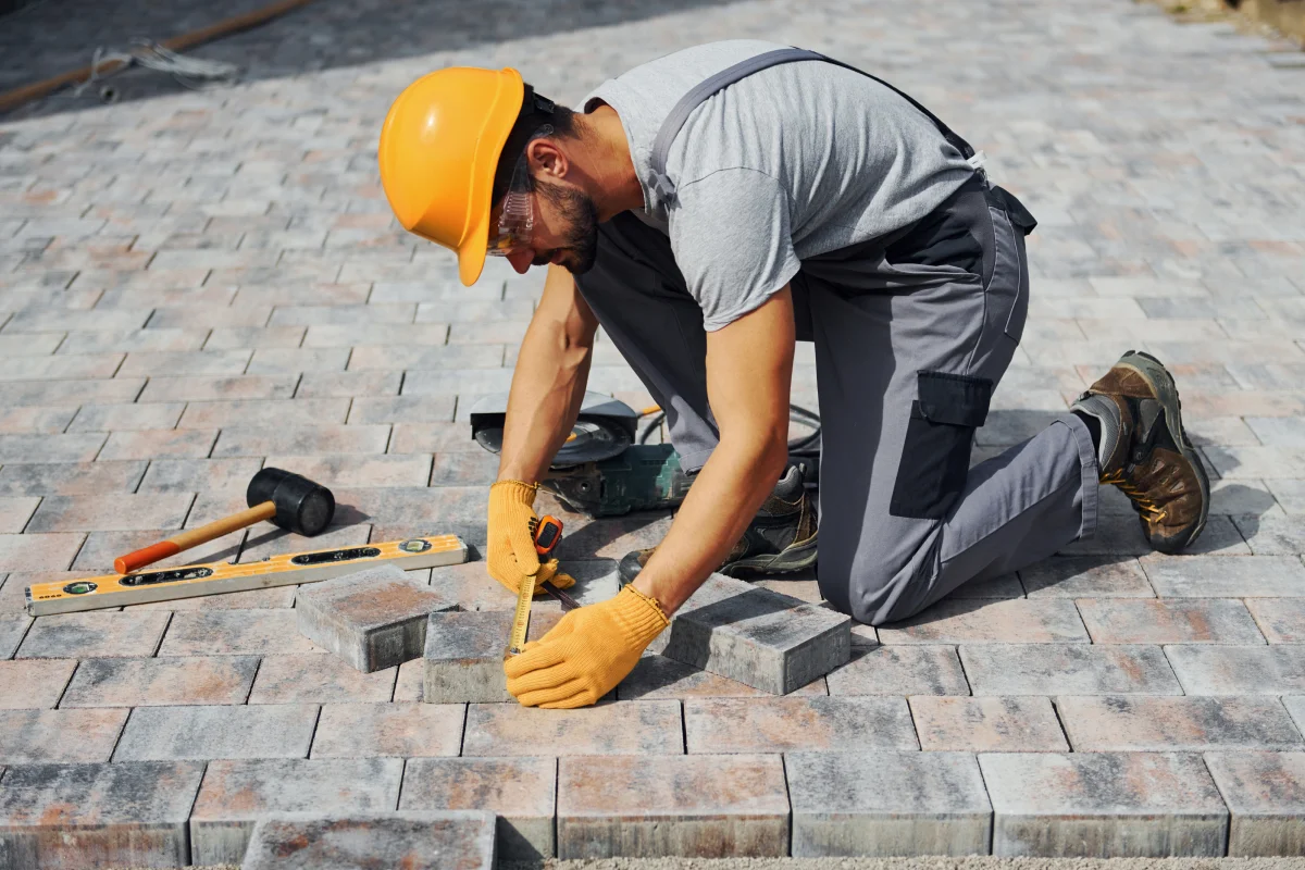 phoenix-landscape-contractor-paver-installation A licensed landscape contractor in a hard hat and safety glasses measuring and setting pavers on a Phoenix, Arizona hardscape project.