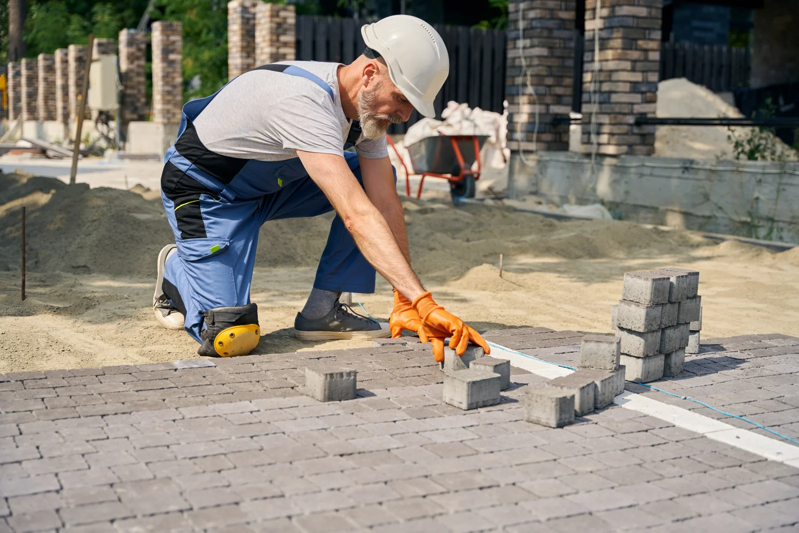 phoenix-landscape-contractor-hardscape-build-in-progress A landscape contractor in a hard hat and knee pads setting concrete pavers on a construction site, part of a hardscape installation project.