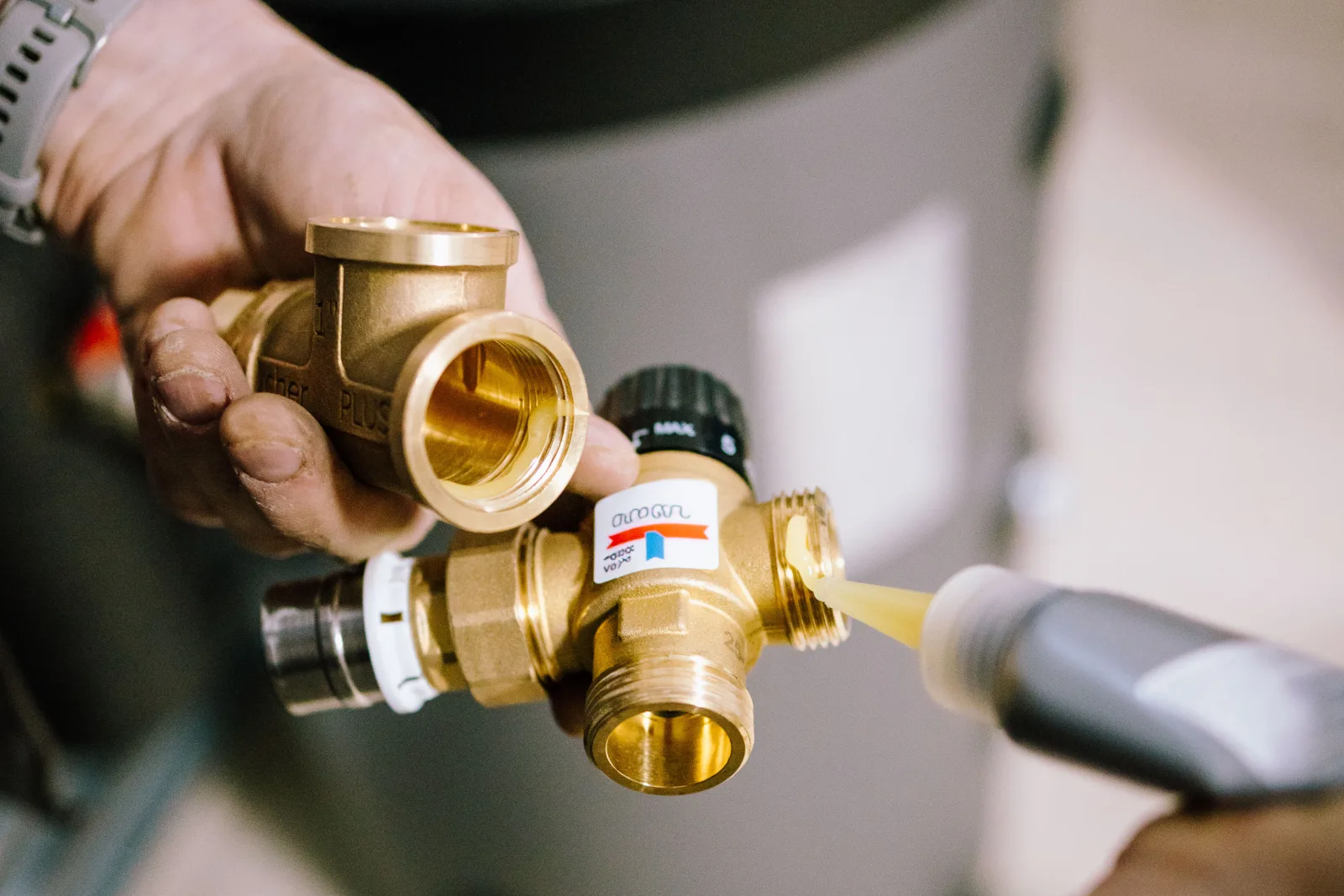 phoenix-plumbing-water-heater-valve A Phoenix plumber applying sealant to a brass pressure-relief valve during a water heater installation.