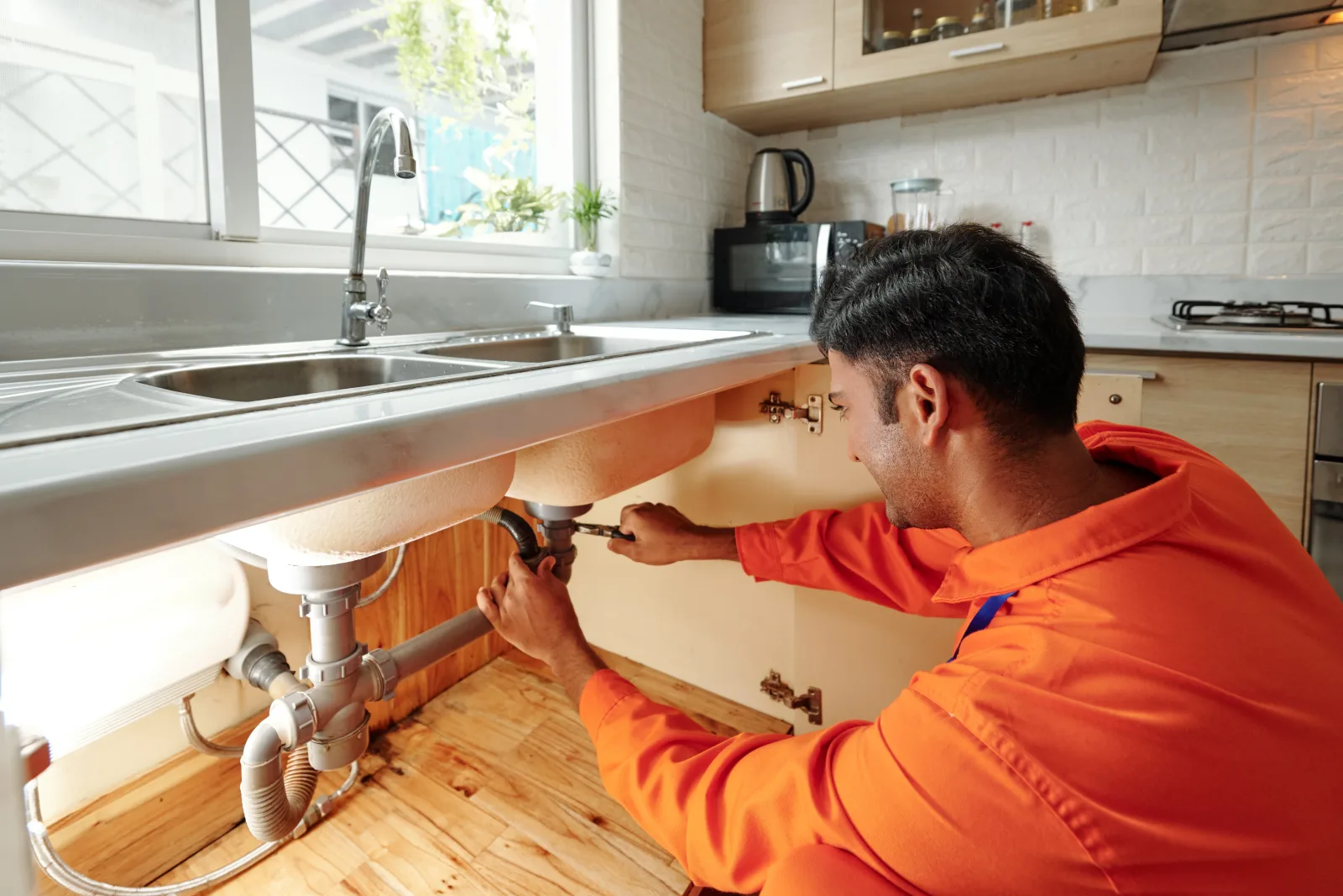 phoenix-plumbing-repair Phoenix plumbing — a licensed plumber in a branded uniform repairing a pipe under a kitchen sink.