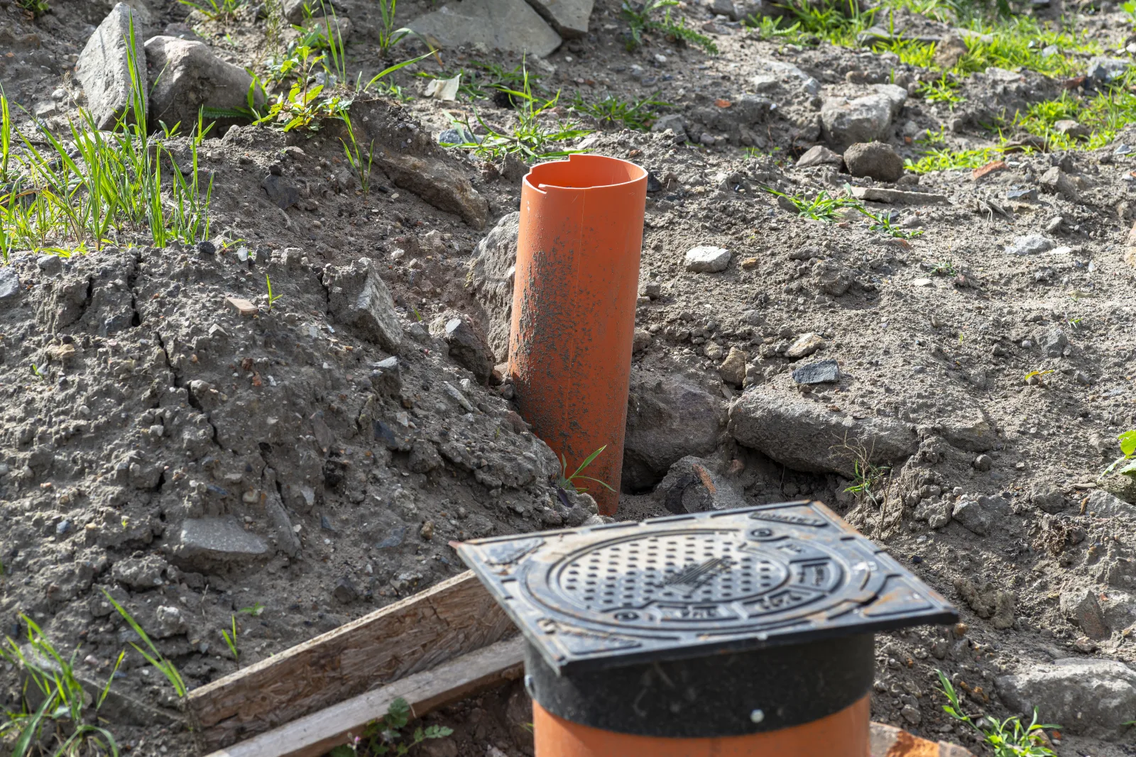 An exterior sewer cleanout pipe with cast cover exposed near a home's foundation, the access point a sewer scope camera is fed through.