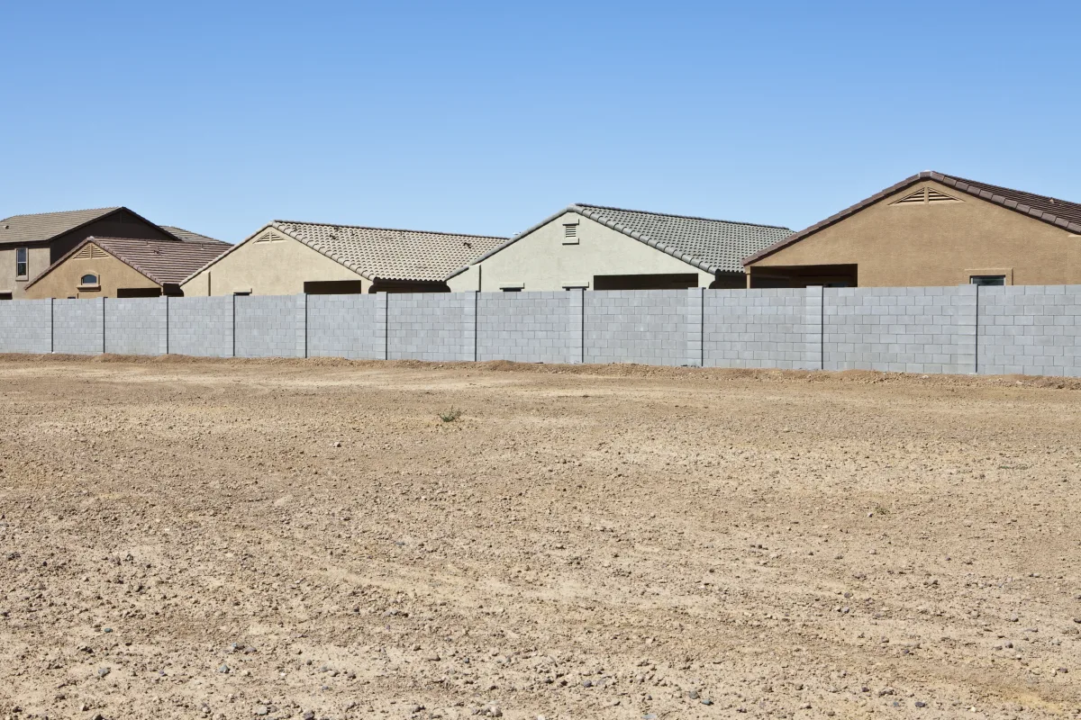 phoenix-snake-removal-desert-block-wall-perimeter Phoenix snake removal — a block wall bordering an undeveloped desert lot behind a Phoenix, Arizona neighborhood, the kind of gap a rattlesnake can use to reach a yard.
