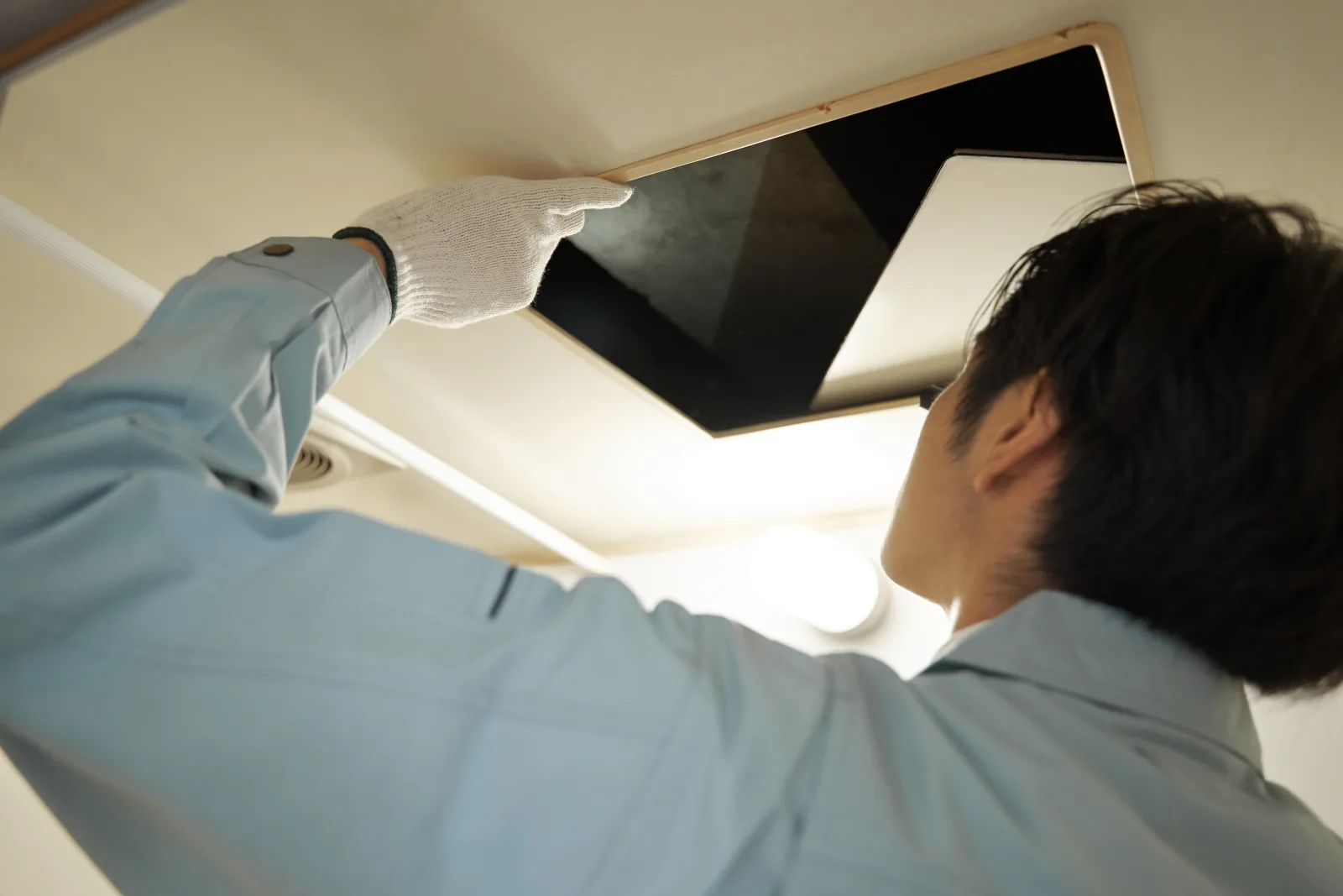 Phoenix wildlife removal — a technician in a work uniform and gloves inspecting an attic access panel for wildlife entry.