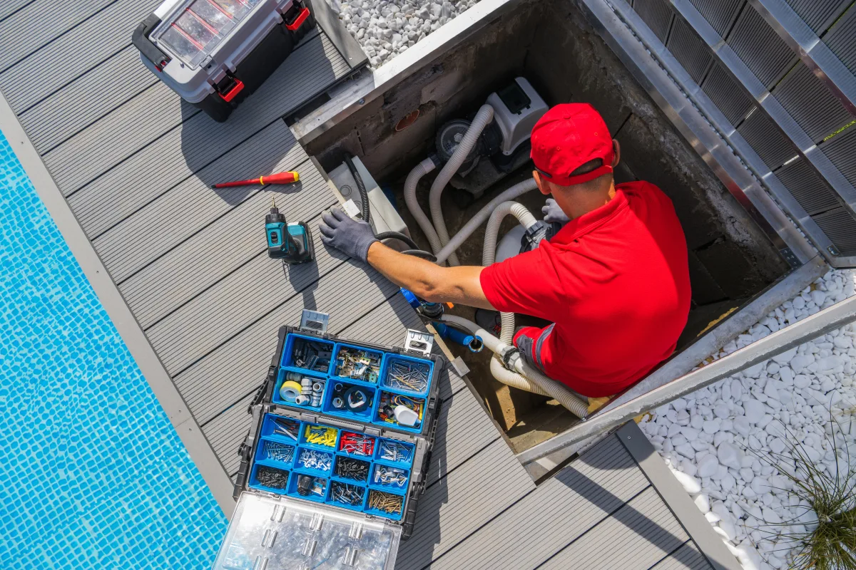 pool-heater-installation-phoenix-technician-poolside-equipment Pool heater installation in Phoenix, Arizona — a pool service technician in a red uniform installing pool heating equipment poolside.