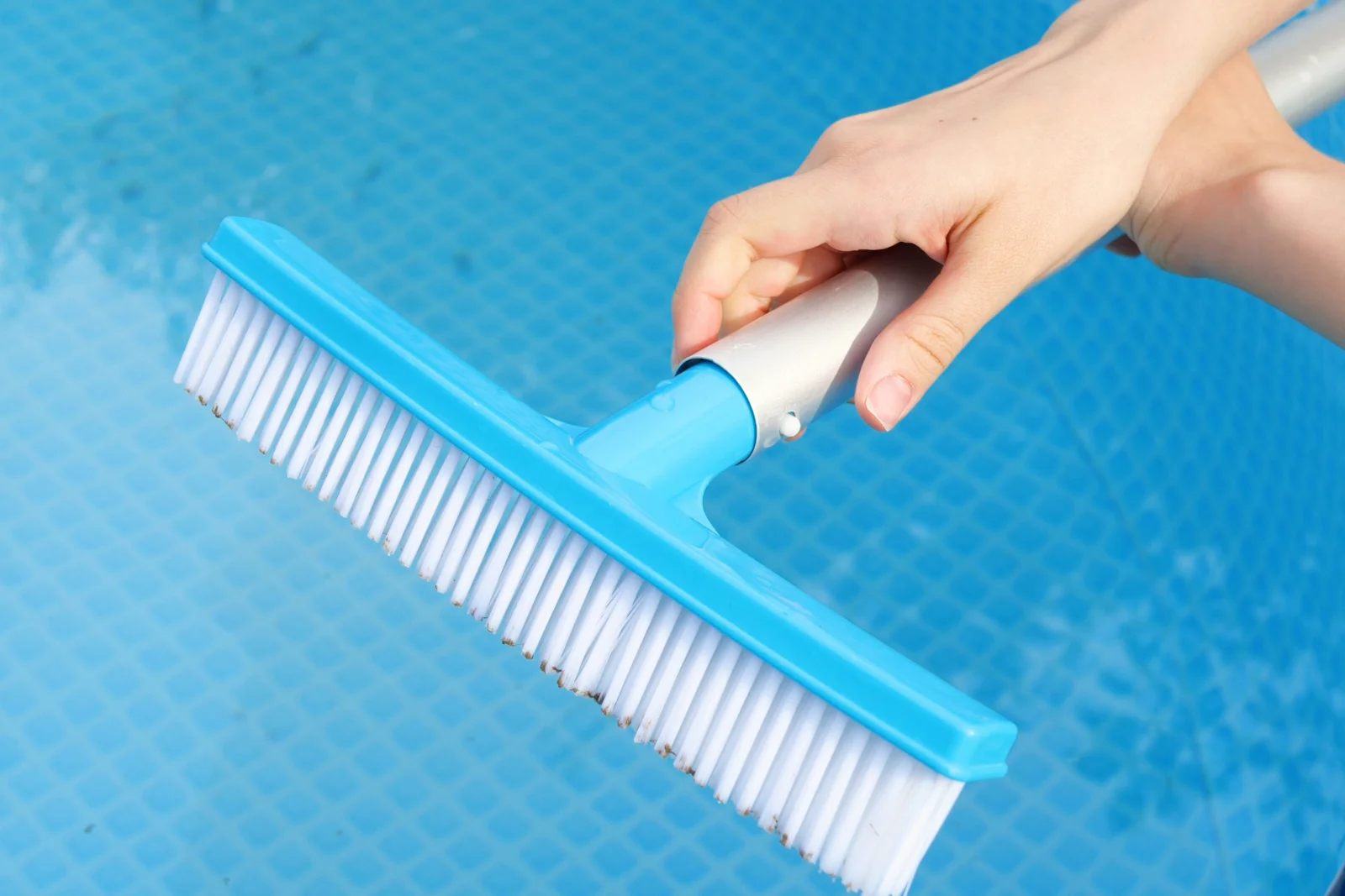 A pool technician brushing the waterline tile of a Phoenix backyard pool between professional calcium-scale cleanings.