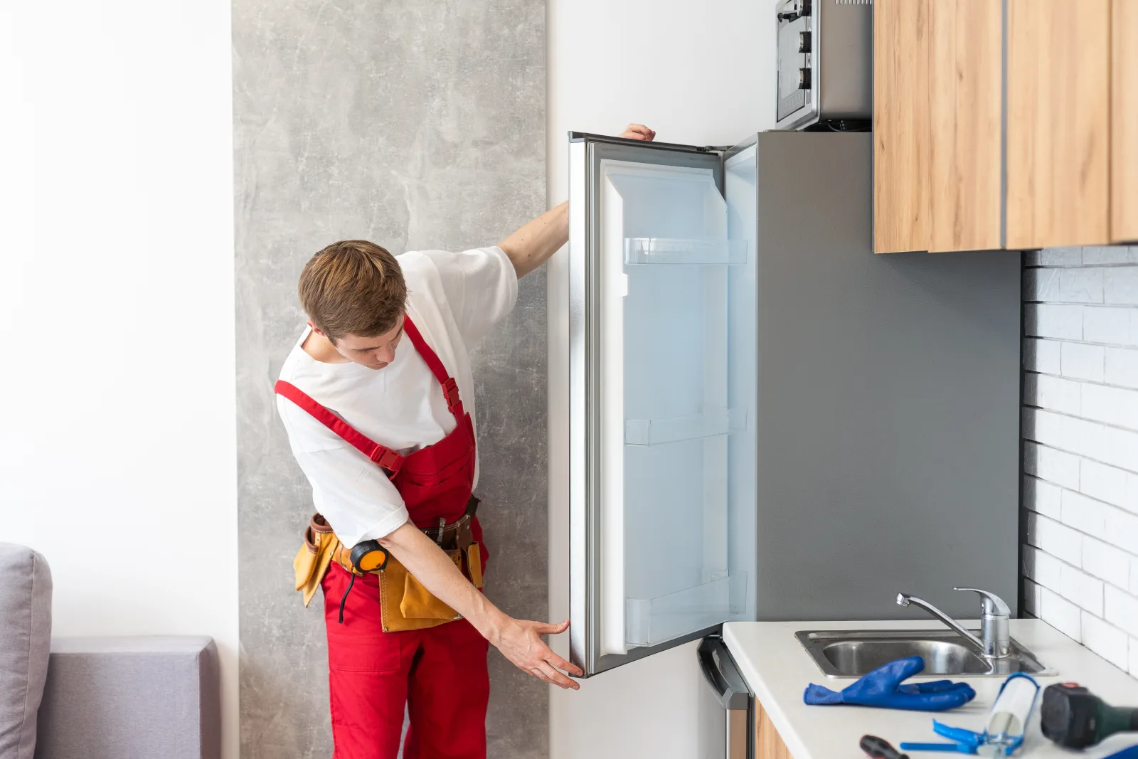 refrigerator-repair-phoenix-desert-conditions A technician in a Phoenix kitchen examining a refrigerator door hinge and seal, the hardware that works hardest to keep cold air in when a home is fighting triple-digit heat outside.