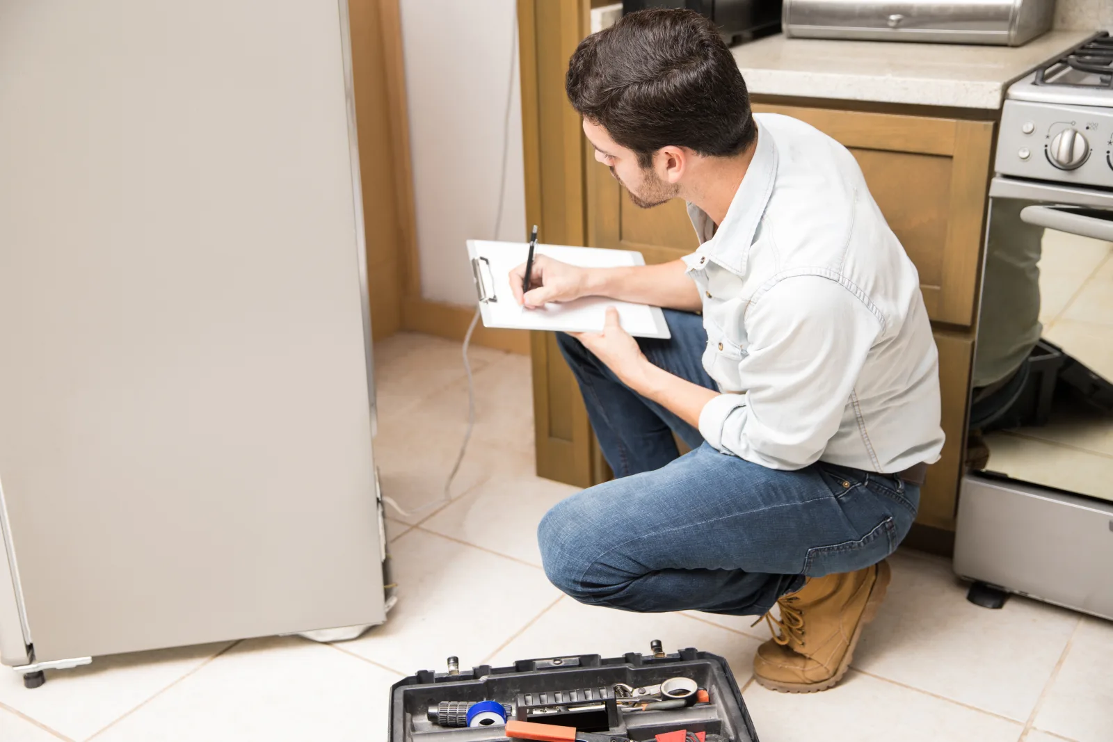 refrigerator-repair-phoenix-technician-diagnosing An appliance technician pulling a refrigerator away from a Phoenix kitchen wall to inspect the condenser coil and compressor before quoting a repair.