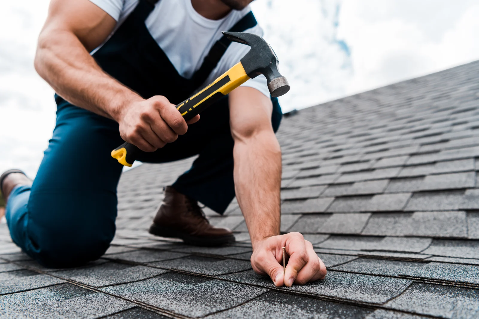 reroofing-phoenix-shingle-installation-close-up Close-up of a roofer's gloved hands hammering a nail into new asphalt shingles during a reroofing job in Phoenix, Arizona.