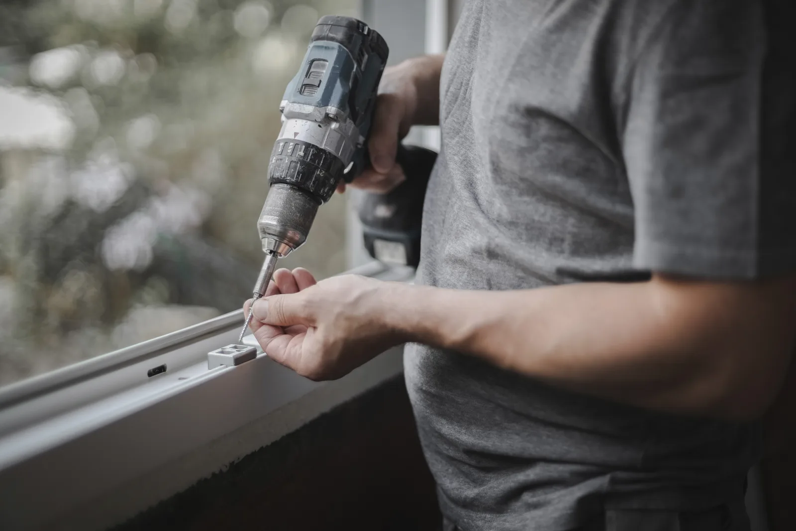Close-up of a drill installing a roller shade mounting bracket into a window frame.
