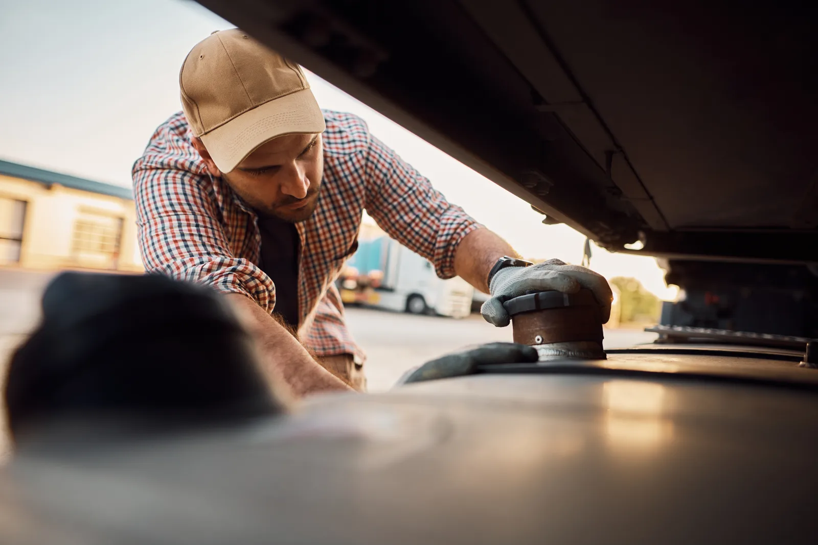 A technician in a ball cap inspecting and resealing an RV roof vent mount with a rotary tool.