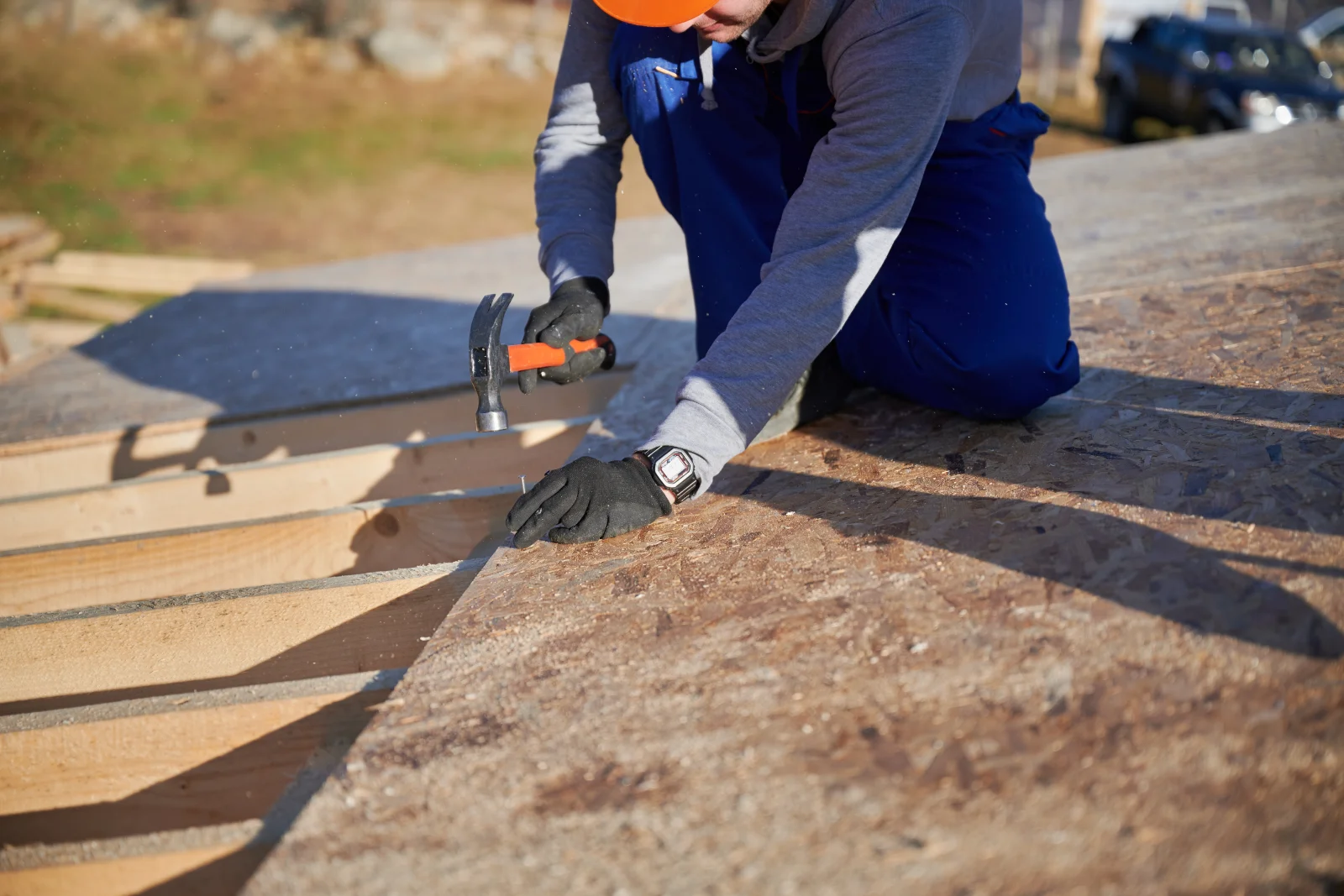 shingle-roof-installation-phoenix-deck-prep A roofing crew member in a hard hat and gloves nailing new OSB decking into place during a shingle roof installation.