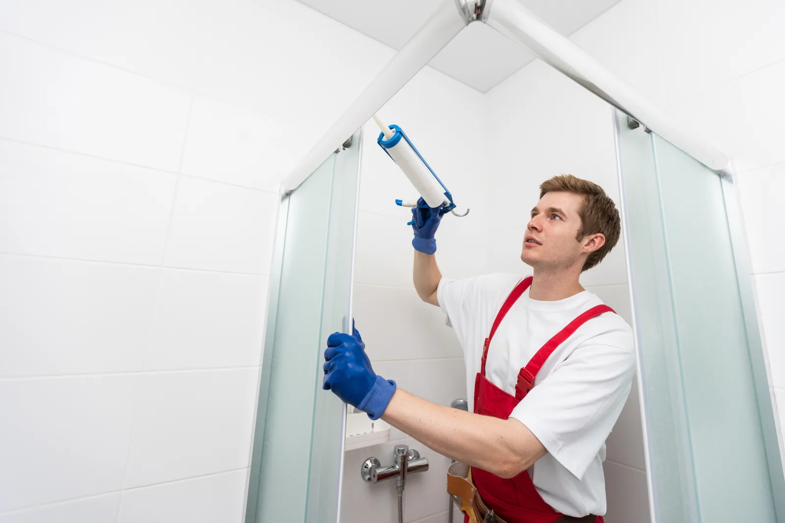 shower-door-installer-phoenix-glass-sealing A professional installer applies a clean silicone seal along the top track of a glass shower door enclosure in a Phoenix, Arizona home to keep the installation leak-free.
