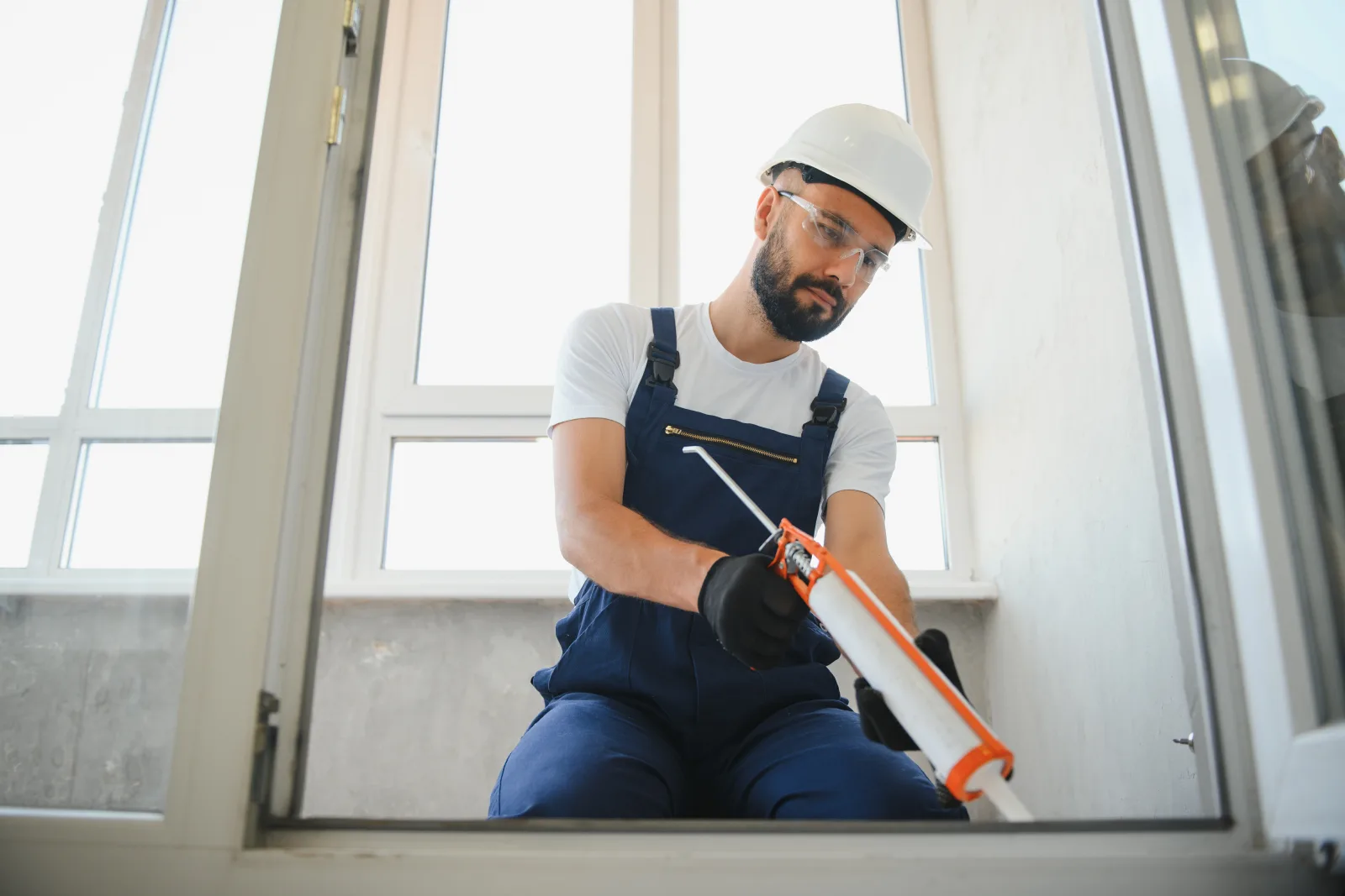 Skylight installation in Phoenix, Arizona — an installer in a hard hat and safety glasses sealing the frame with silicone to keep out monsoon rain.