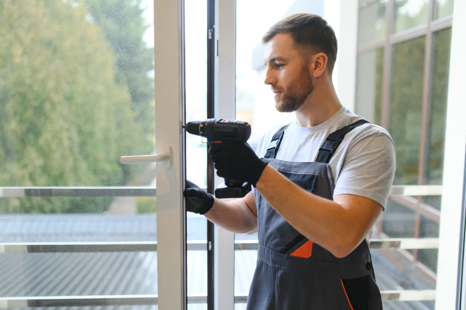 sliding-door-repair-phoenix-technician-adjusting-door-hardware Sliding door repair in Phoenix, Arizona — a technician in coveralls using a drill to adjust the hardware on a sliding glass patio door.