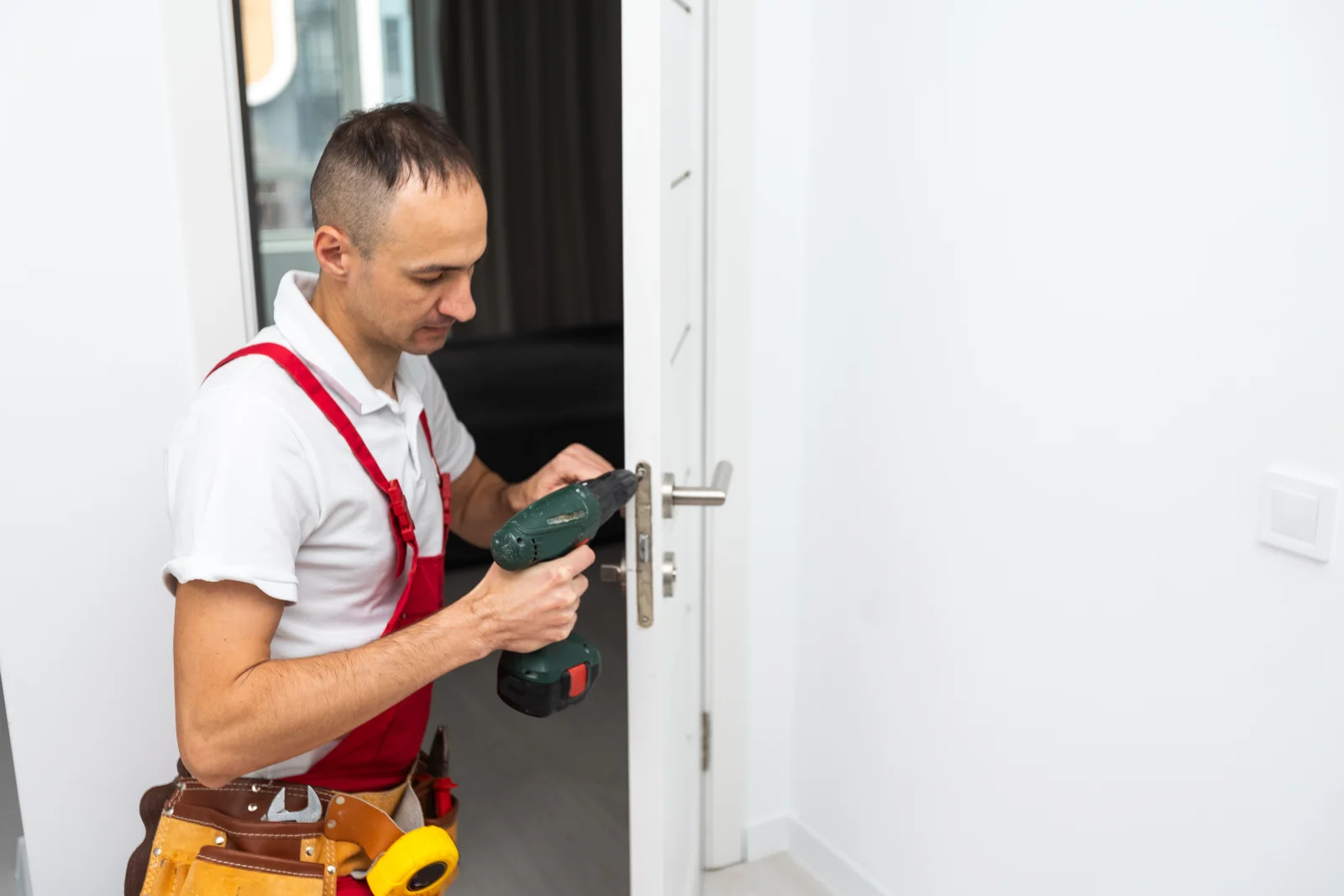 smart-lock-installation-phoenix-drill-install-technician A technician in a work uniform and tool belt using a cordless drill to install a smart lock on an interior door edge in a Phoenix home.