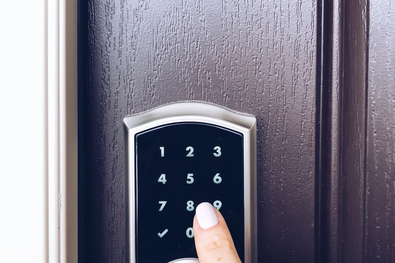 smart-lock-installation-phoenix-keypad-entry-touchscreen A close-up of a finger entering a code on a digital touchscreen keypad deadbolt on a dark exterior door in Phoenix.